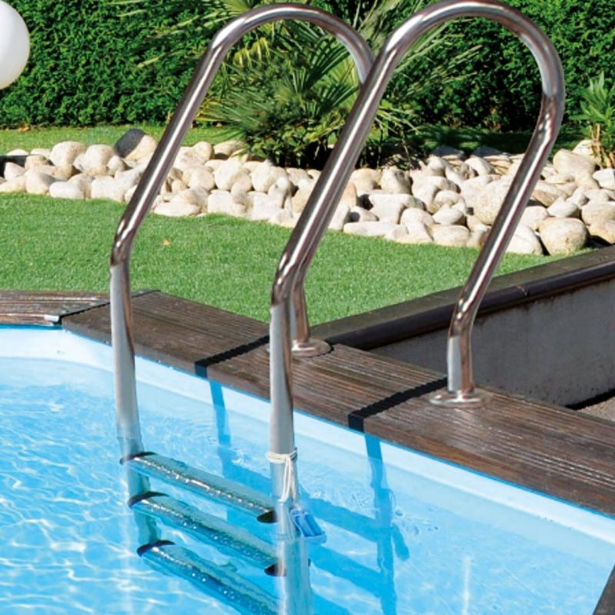 Escalera de acero inoxidable en una piscina, rodeada de césped y piedras.