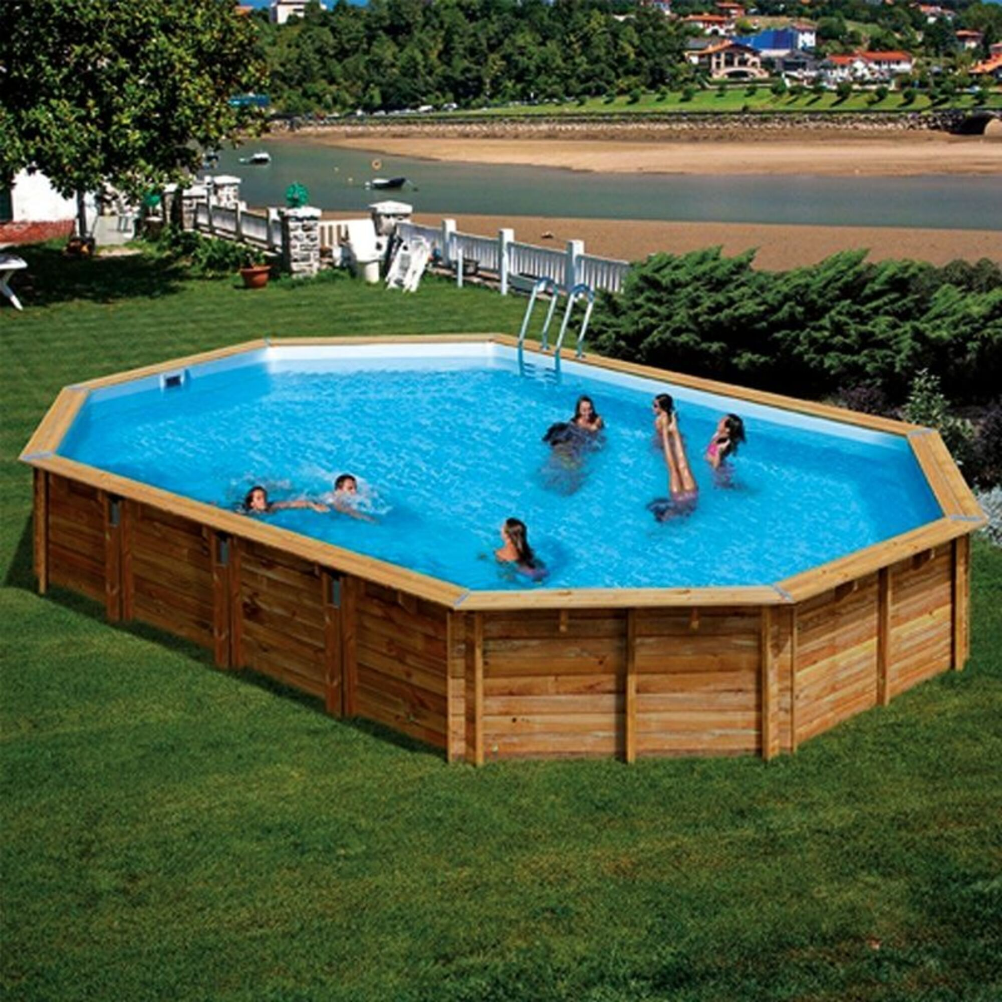 Niños chapotean en una piscina octogonal de madera en un jardín con vistas al mar.