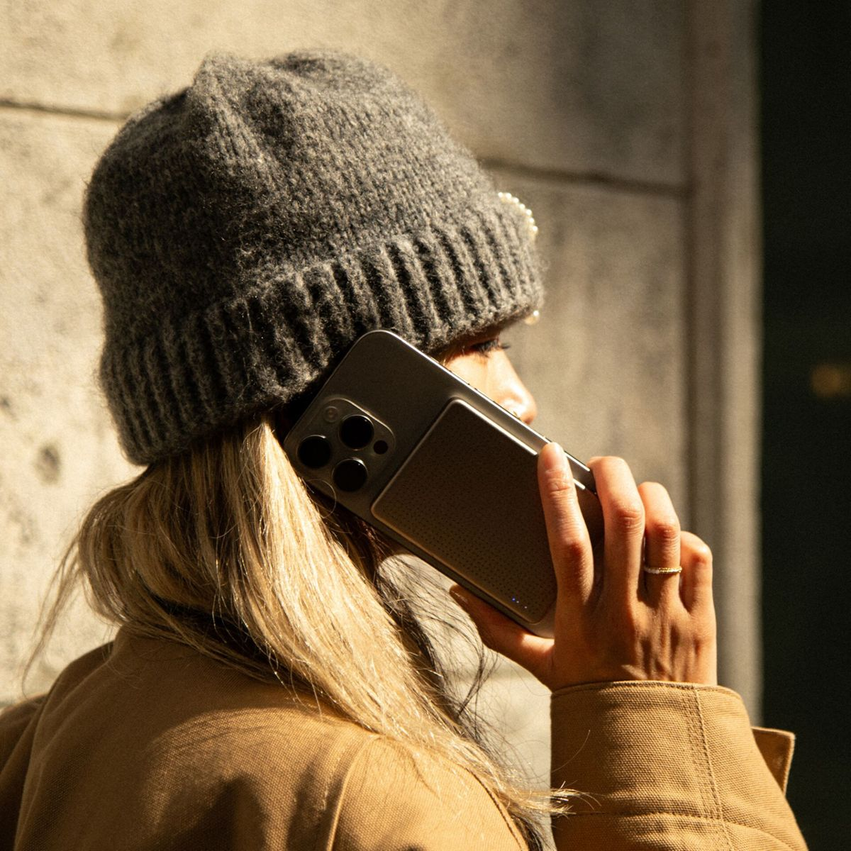 Femme en bonnet gris et manteau beige parlant au téléphone à triple caméra.