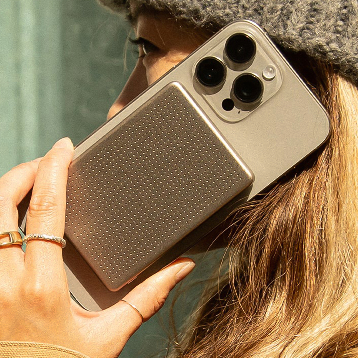 Une personne portant un bonnet tient un téléphone avec un dos texturé. Gros plan sur l'oreille et la caméra.