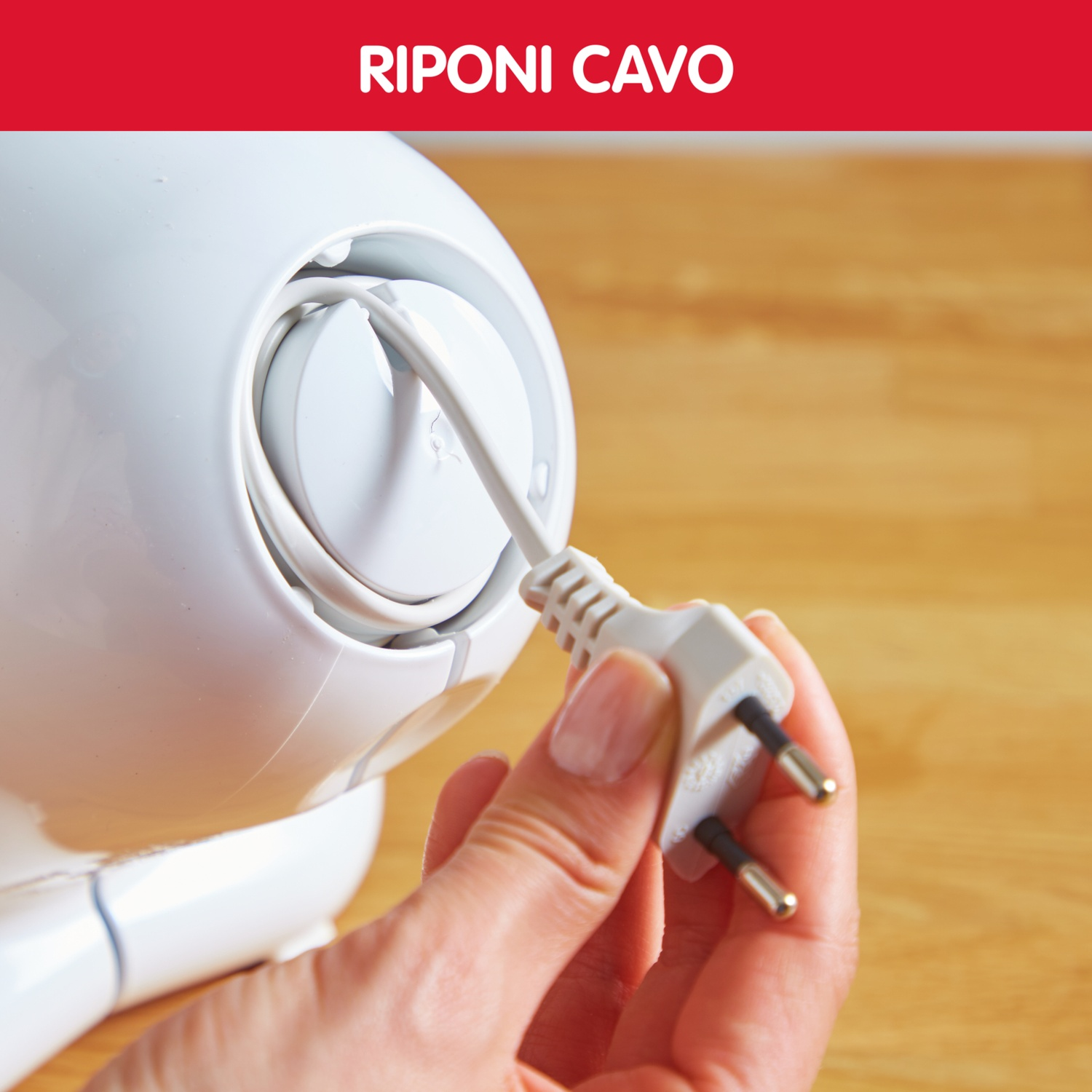 Una mano tiene una spina elettrica bianca accanto a un elettrodomestico bianco con cavo avvolto.
