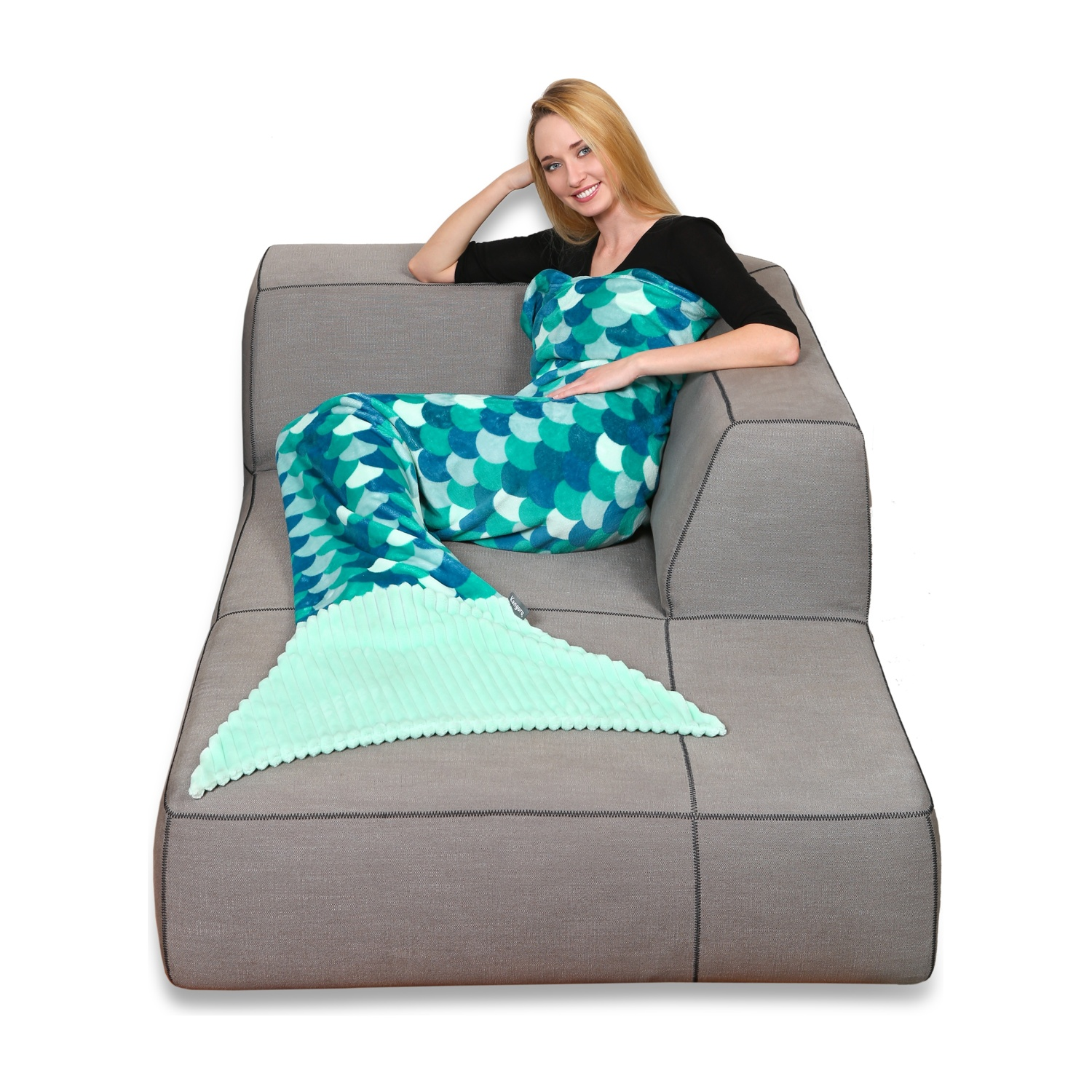 Donna su un divano con coperta a coda di sirena, sorridente.