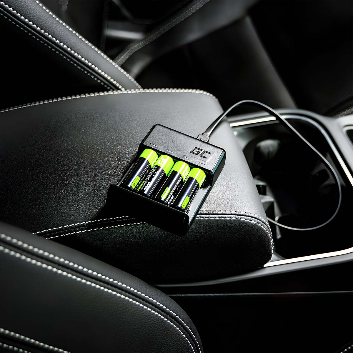 Un caricabatterie nero con quattro batterie AA verdi è collegato sul bracciolo di un'auto.