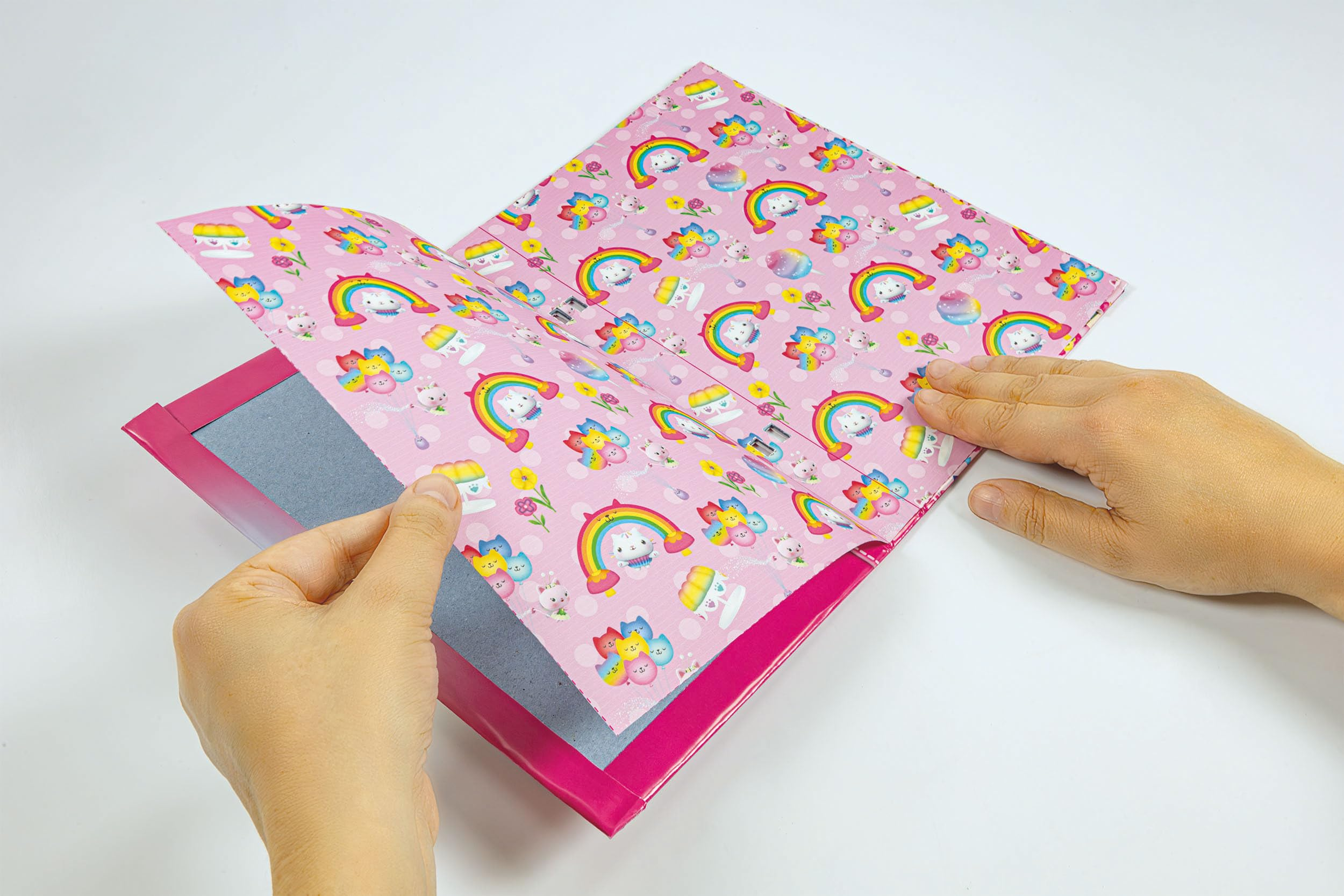 Mani che tengono carta rosa con gatti, arcobaleni, fiori e cupcake.