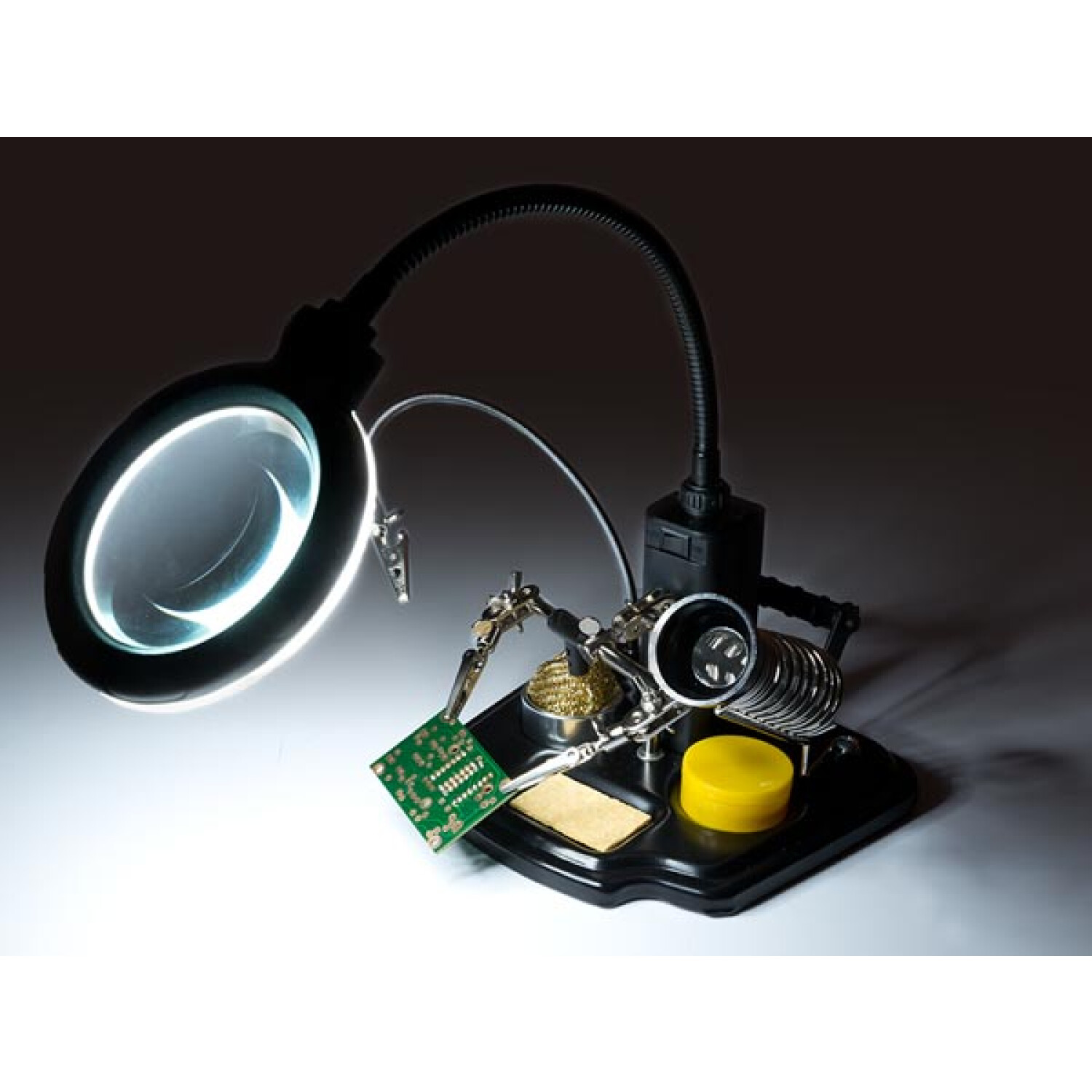 Stazione di saldatura con lampada d'ingrandimento, pinza e circuito stampato.