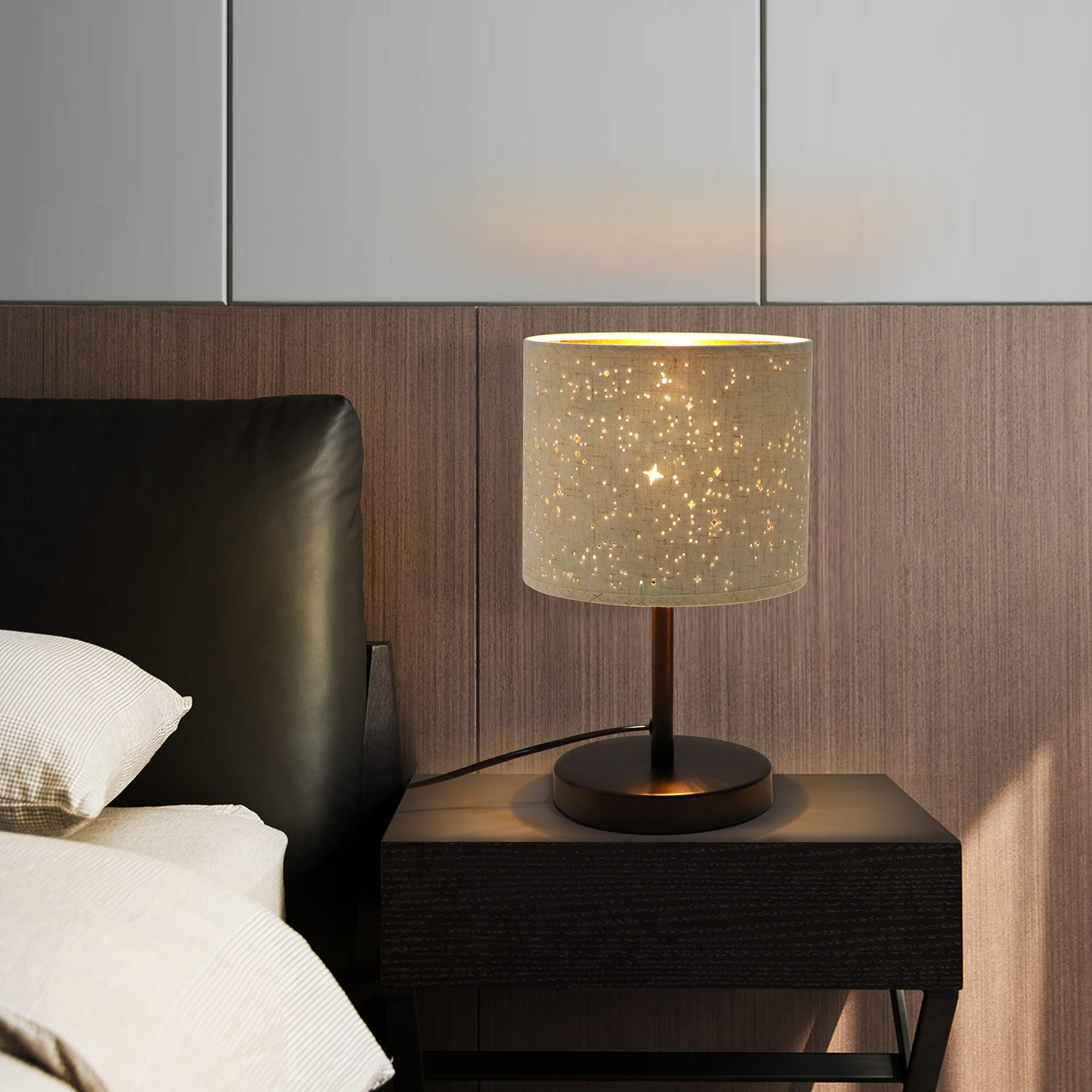 Una lampada da comodino con motivo a stella siede su un comodino scuro accanto a un letto.