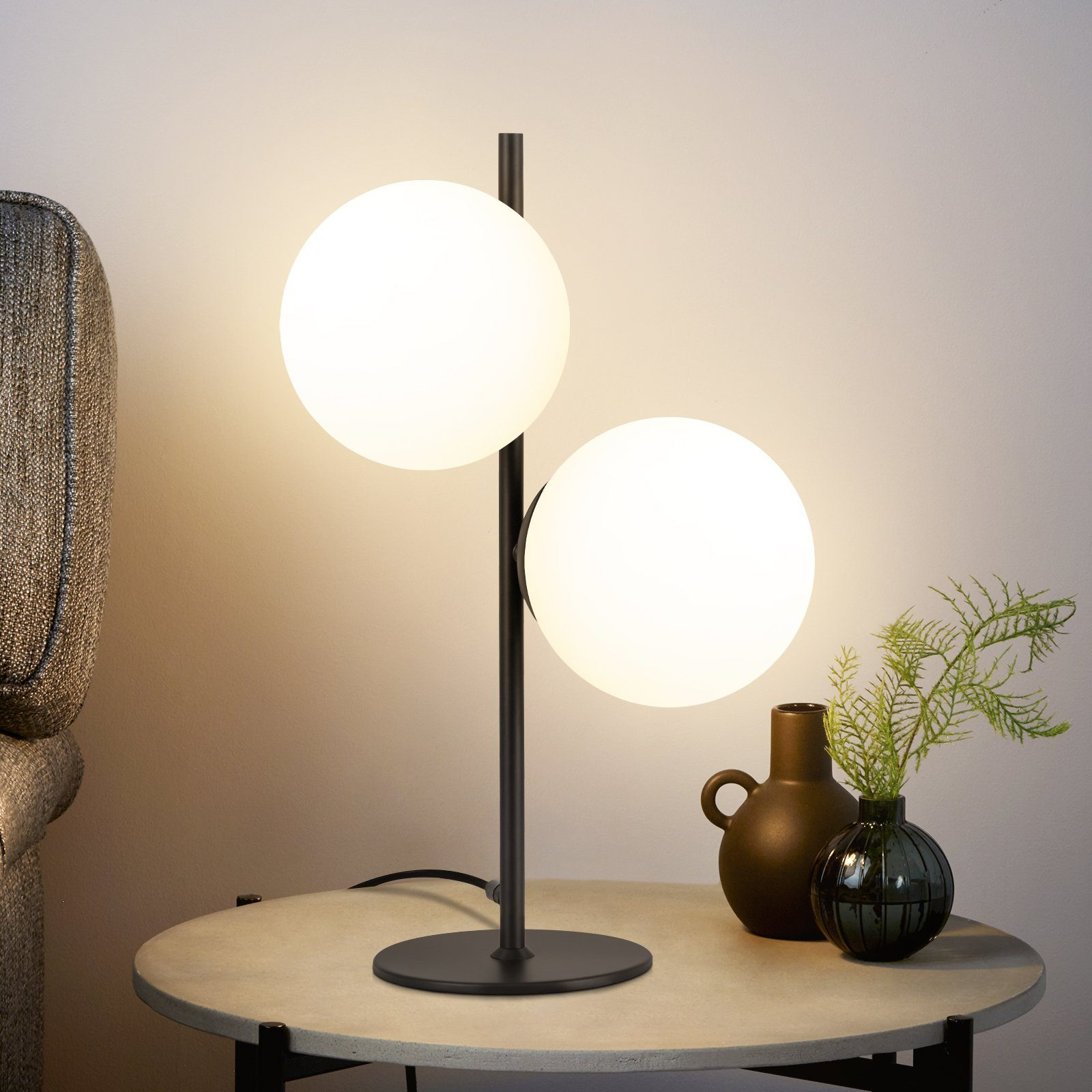 Eine moderne Tischlampe mit zwei Kugelleuchten auf einem runden Tisch.