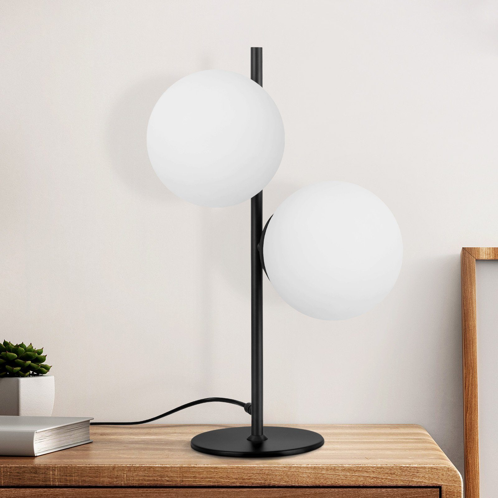 Eine schwarze Tischlampe mit zwei weißen Kugelleuchten auf einem Holztisch.