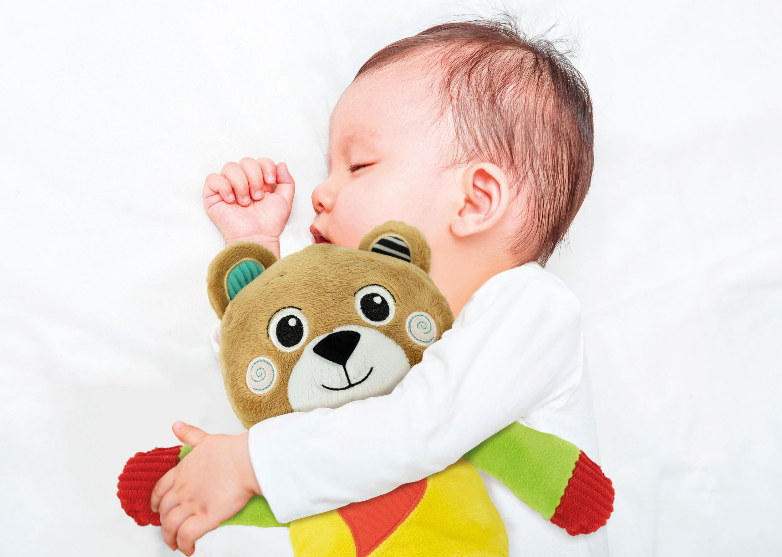 Un bambino dorme pacificamente abbracciando un orsacchiotto di peluche su un letto bianco.