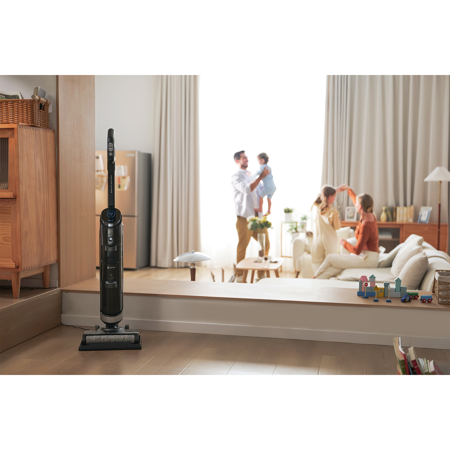 Czarny odkurzacz stoi na drewnianej podłodze. Rodzina bawi się w tle.