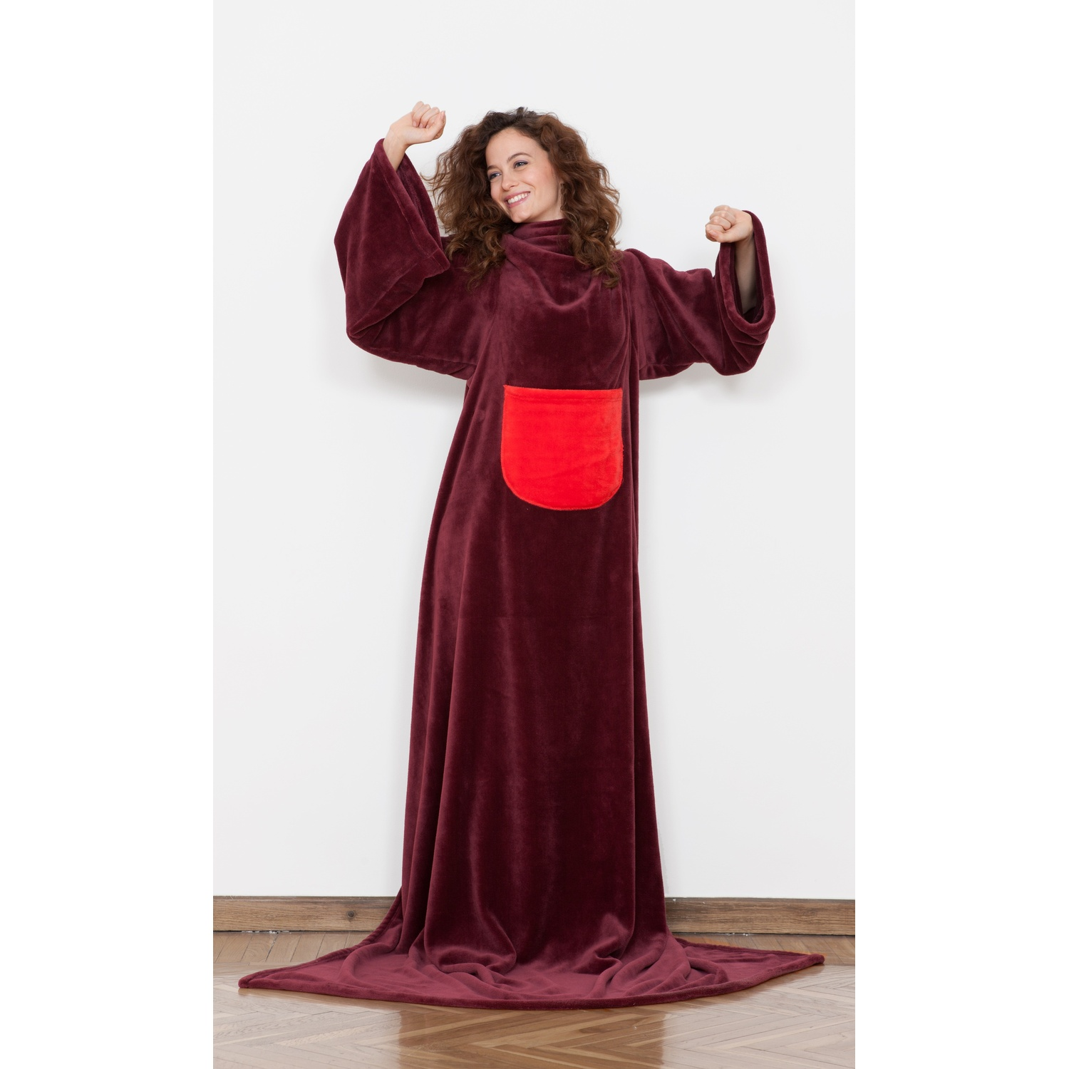 Donna in vestaglia bordeaux con tasca rossa alza le braccia, sorridendo.