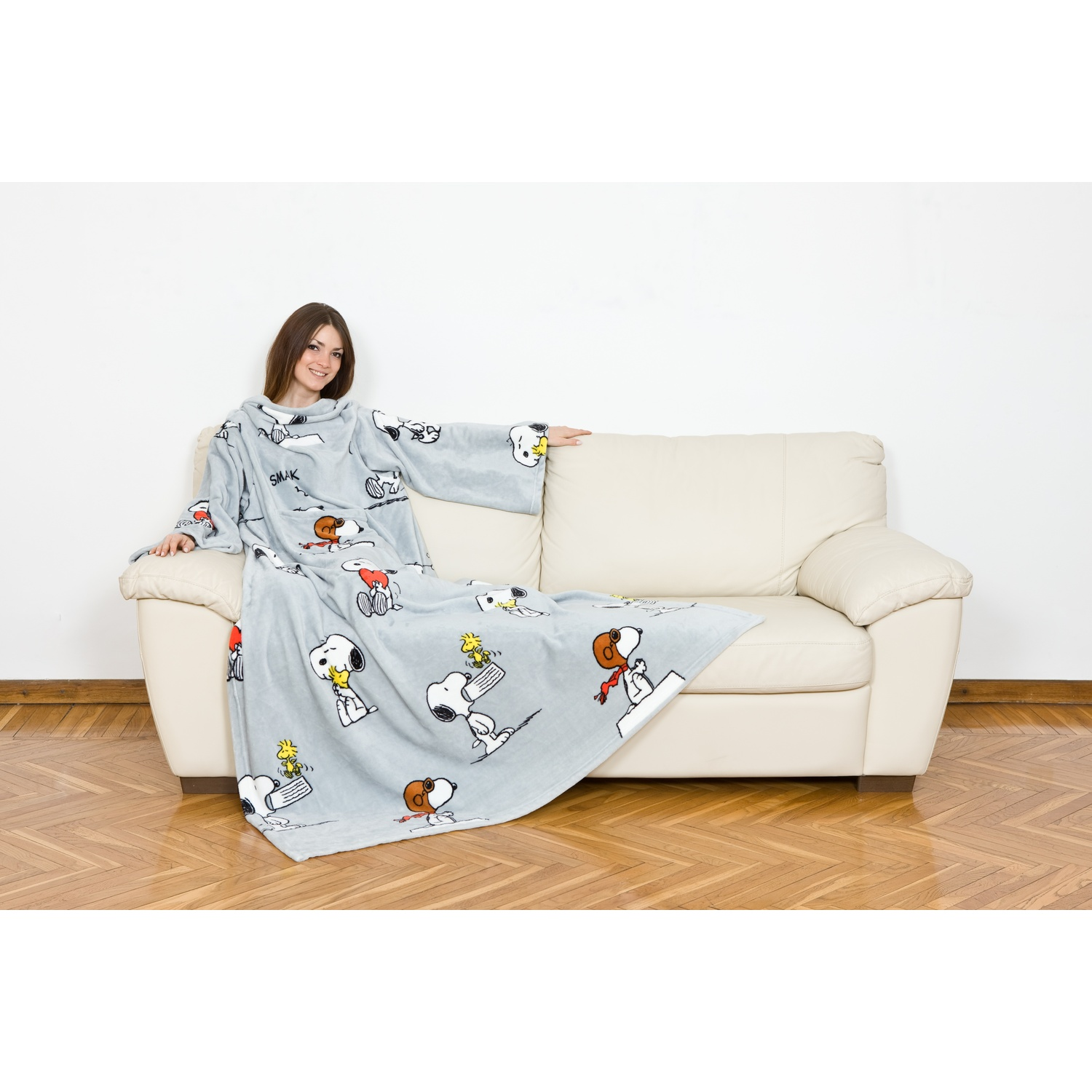 Donna su un divano indossa una coperta grigia con personaggi di Snoopy. Accogliente e rilassata.