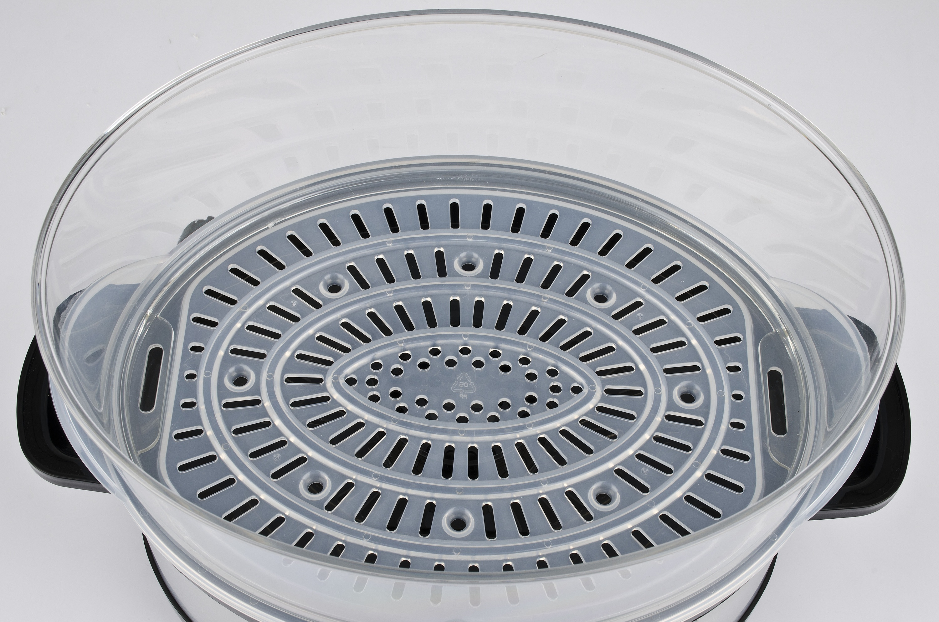 Un inserto per vaporiera in plastica trasparente con fessure e fori su sfondo grigio.