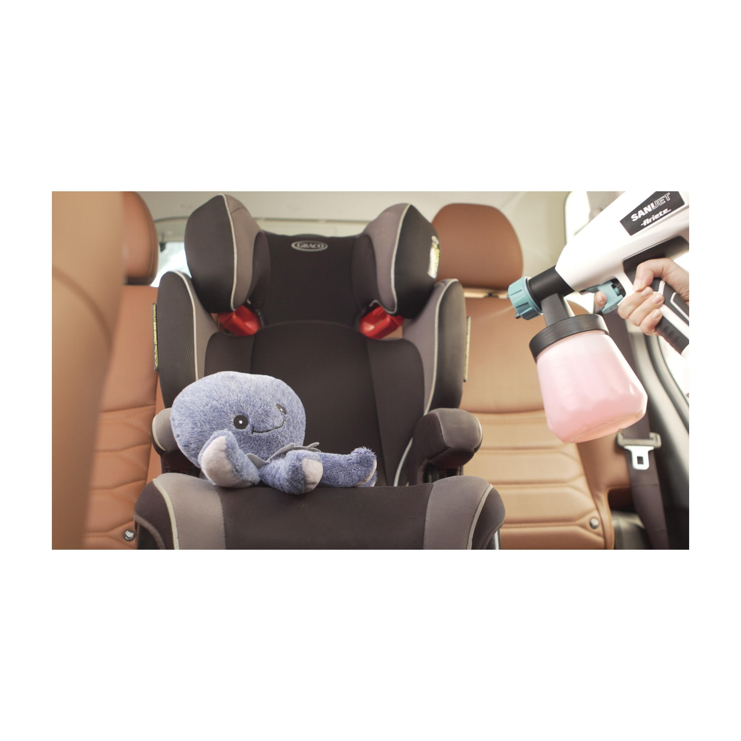 Un polpo di peluche blu è seduto su un seggiolino auto. Una mano tiene una pistola spray disinfettante.