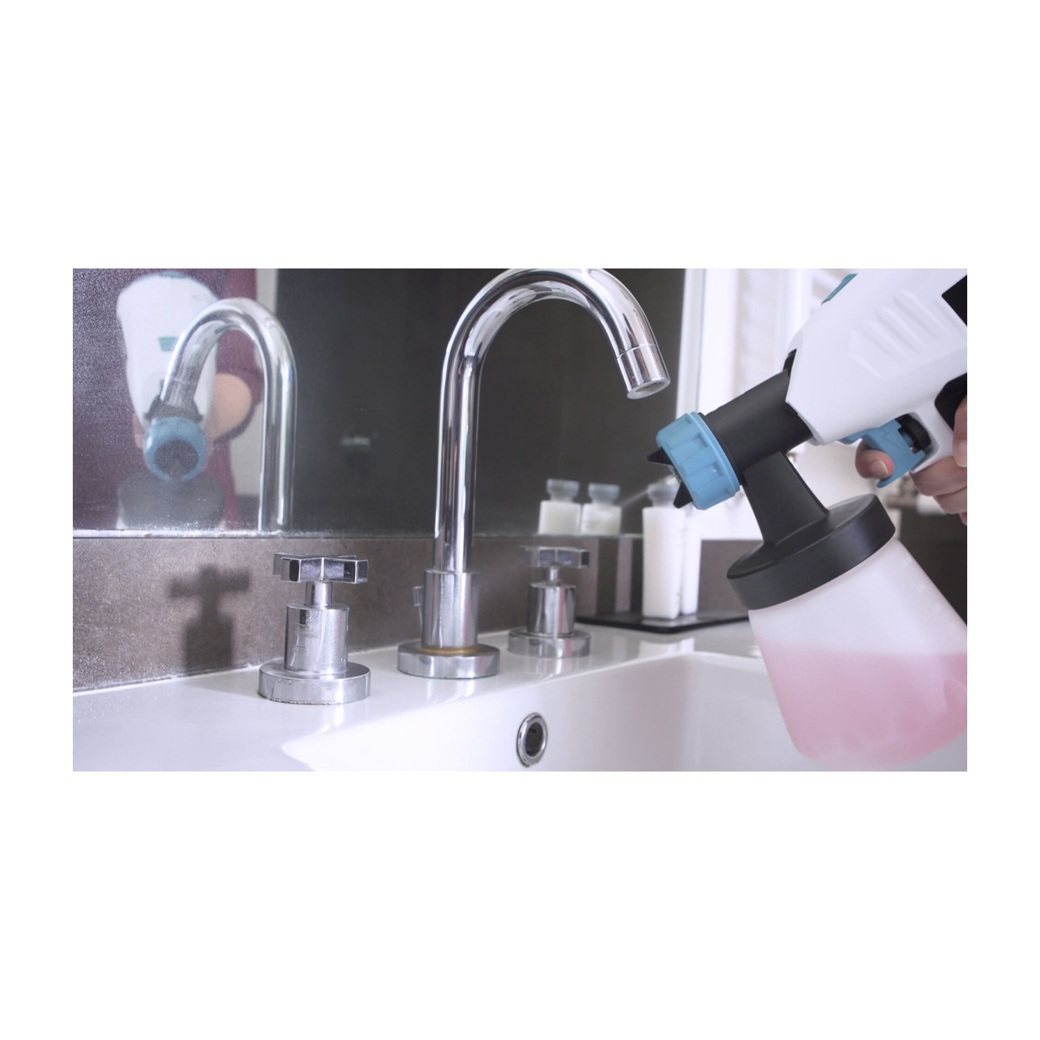 Una mano tiene una bottiglia spray bianca con liquido rosa sopra un lavandino.
