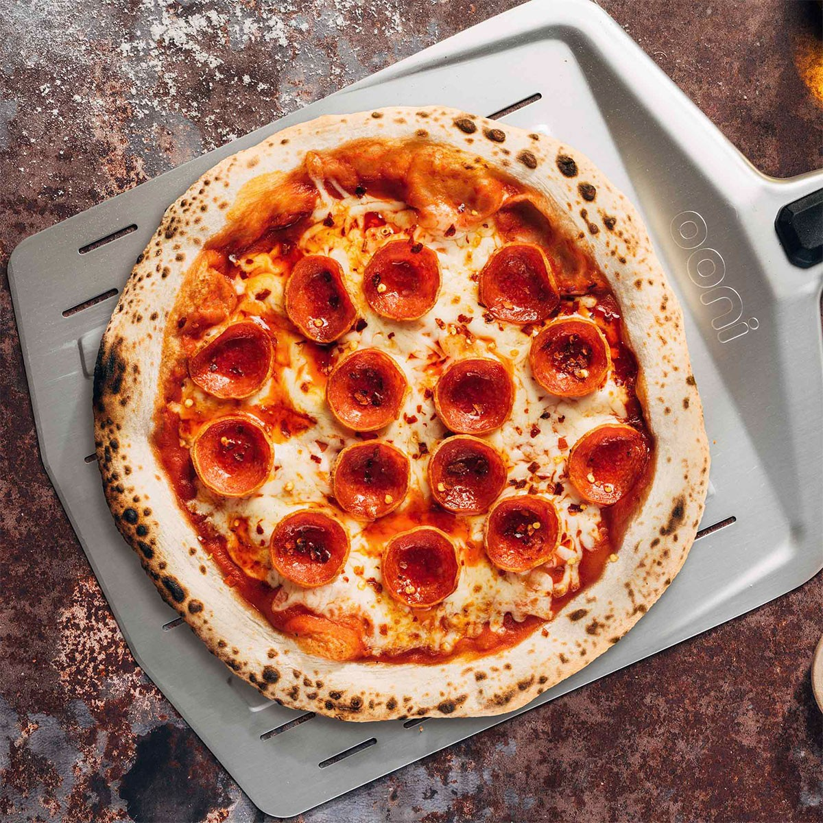 Una pizza al salame piccante con formaggio fuso si trova su una pala per pizza con sfondo rustico.