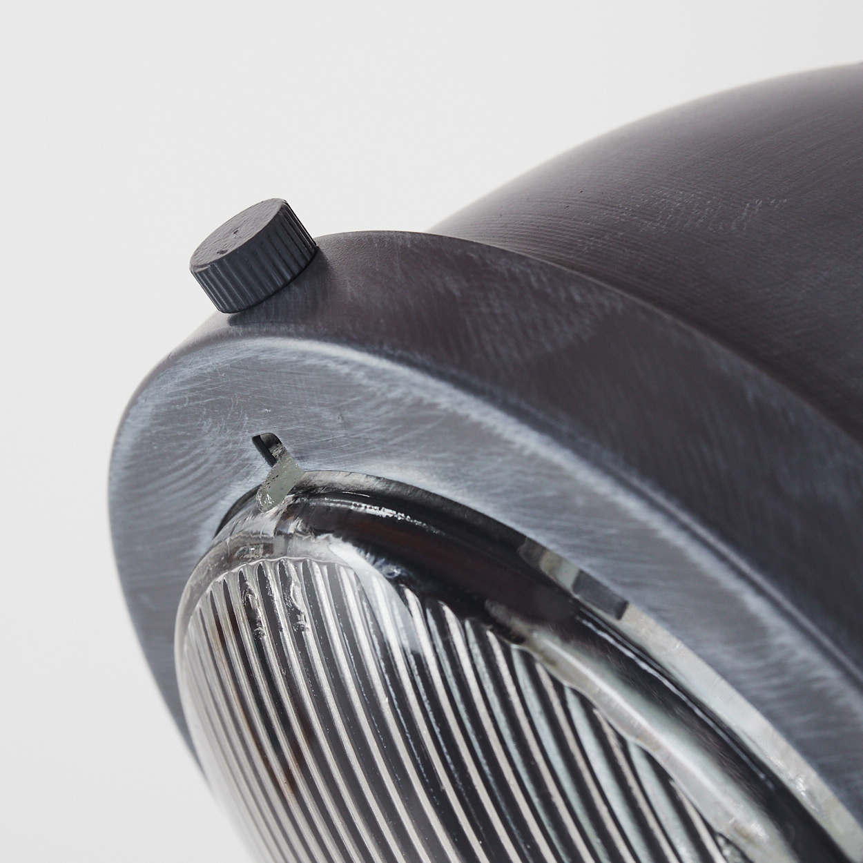 Nahaufnahme einer dunklen, runden Lampe mit geriffeltem Knopf und Glaslinse.