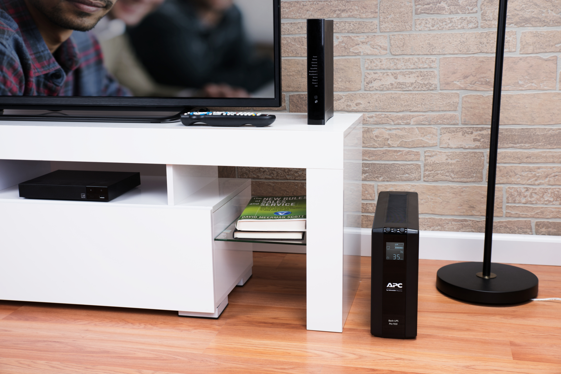 Eine schwarze USV steht auf einem Holzboden neben einer weißen Medienkonsole mit TV und Büchern.