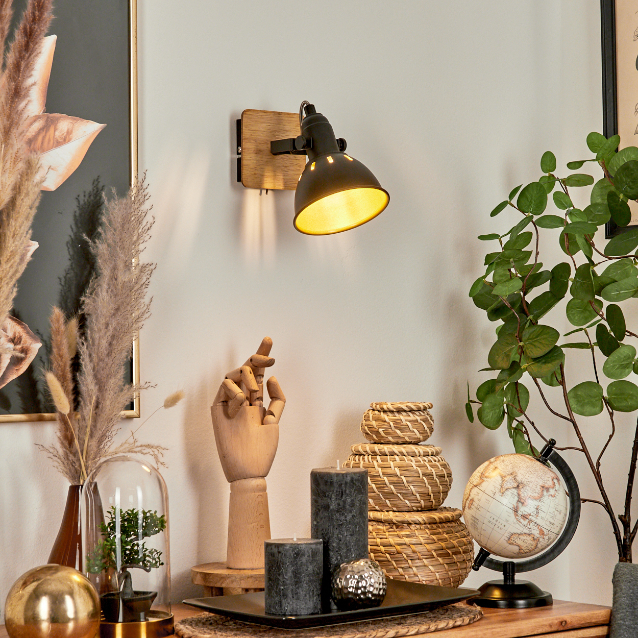 Eine Wandleuchte beleuchtet eine Vignette mit hölzerner Hand, Kerzen, Körben und Globus.