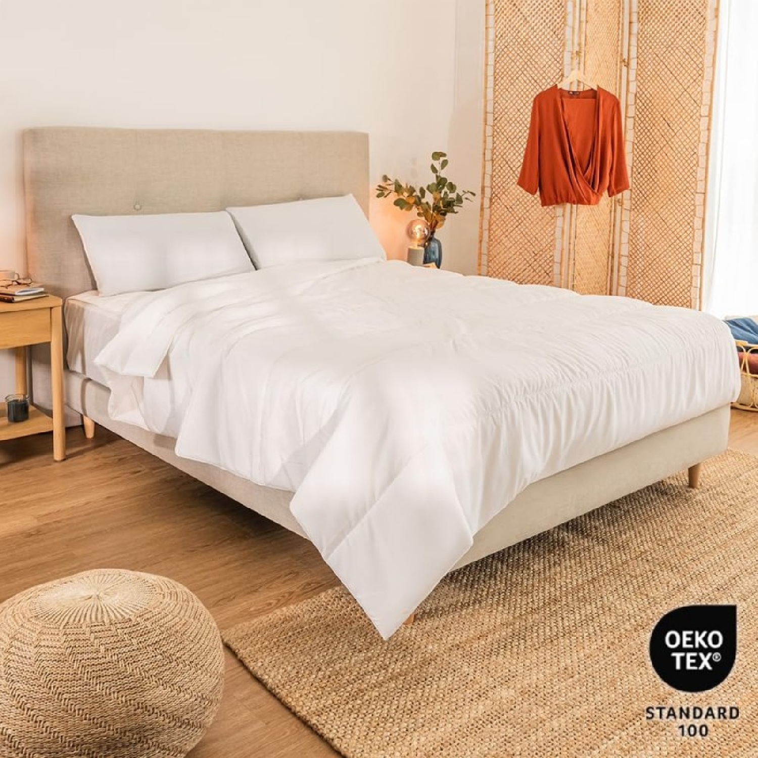 Un letto ben fatto con lenzuola bianche, testiera beige e divisorio per ambienti intrecciato.