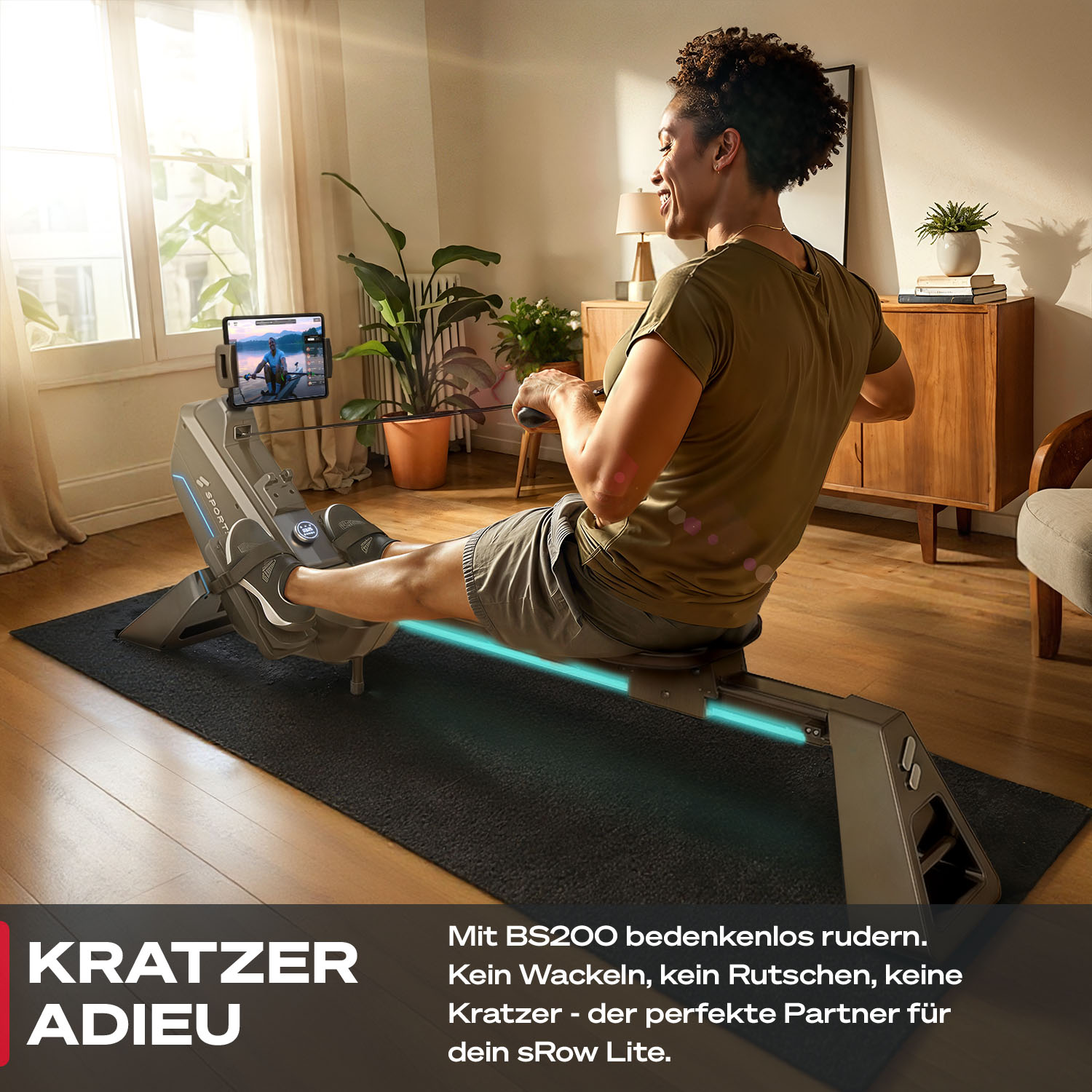 Eine Frau rudert auf einem Ergometer in einem Wohnzimmer, das Tablet zeigt ein Trainingsvideo.