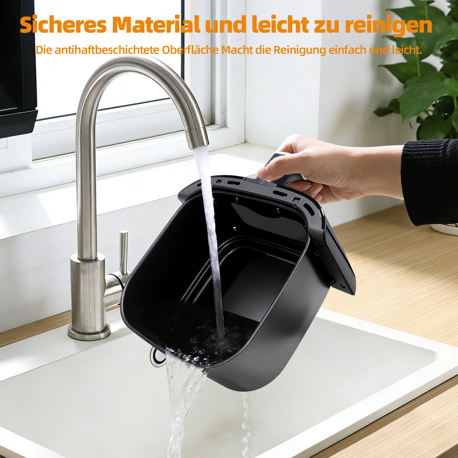 Eine Hand spült einen schwarzen Airfryer-Korb unter fließendem Wasser in einem weißen Waschbecken.