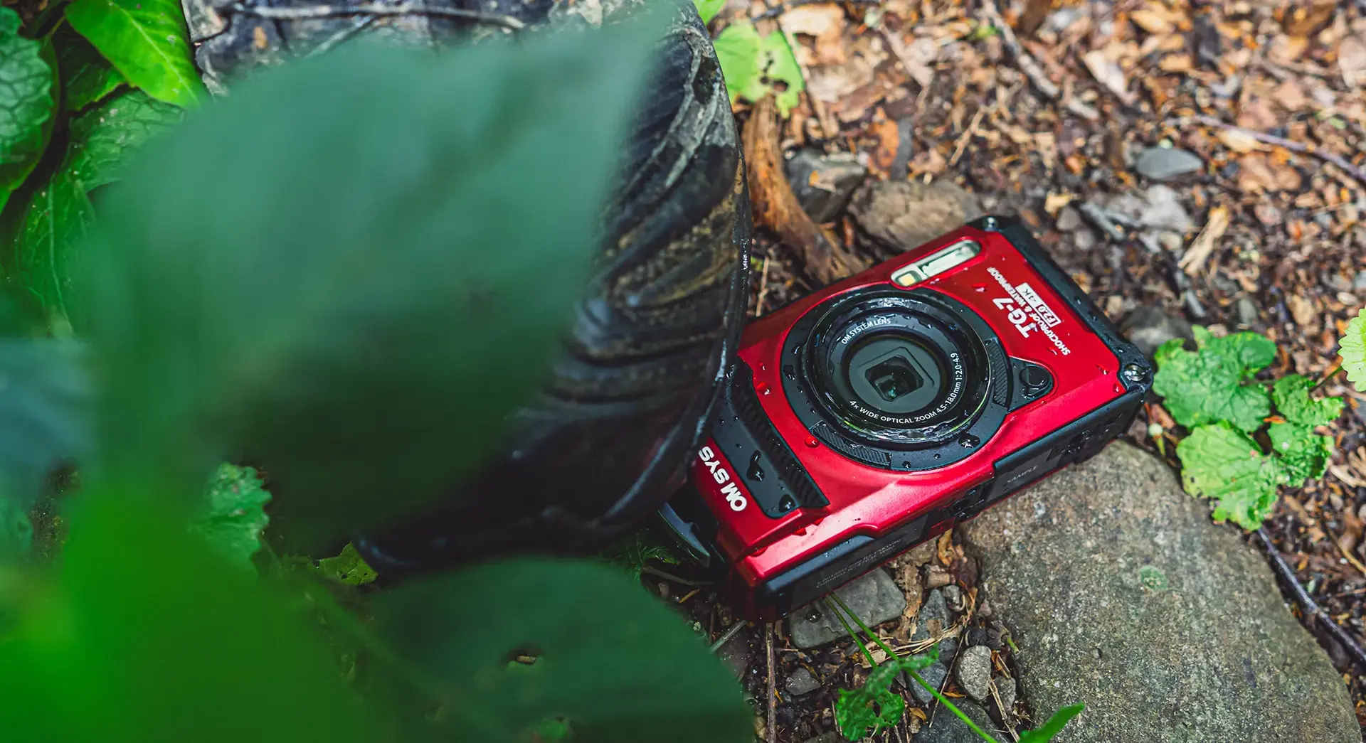 Una cámara roja OM System TG-7 descansa en el suelo junto a una bota.