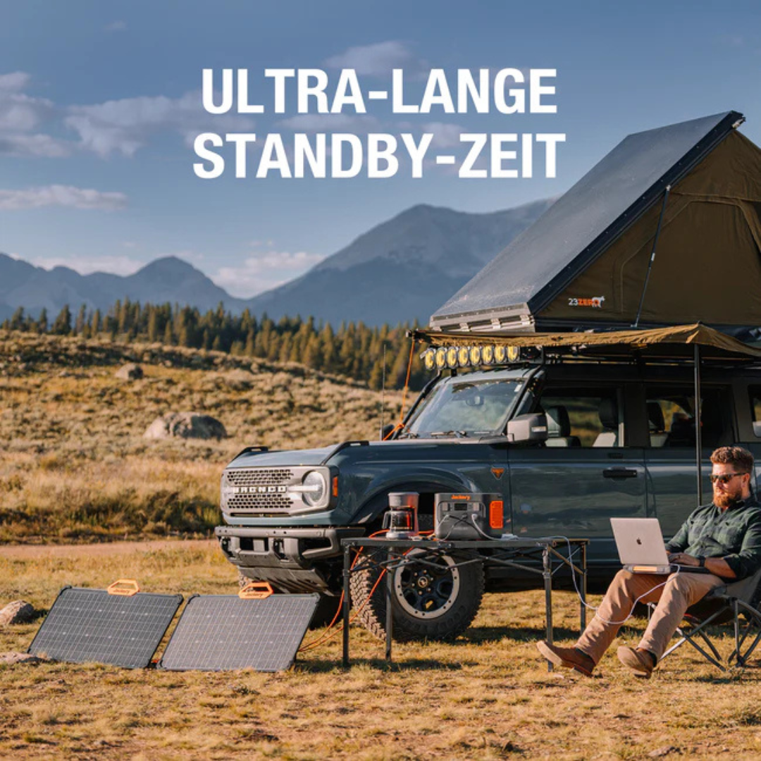 Mann sitzt neben SUV mit Dachzelt, benutzt Laptop. Solarpanels versorgen Geräte.