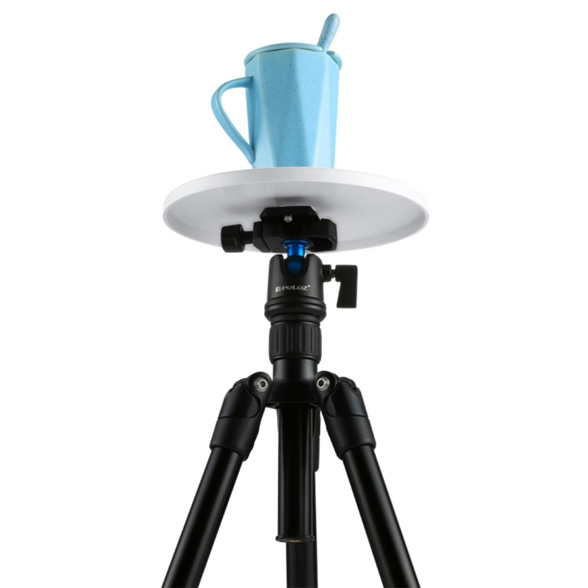 Una tazza blu maculata con cucchiaio poggia su un piatto bianco sopra un treppiede nero.