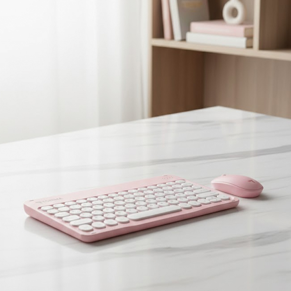 Mermer bir masanın üzerindeki pembe klavye ve fare, kitaplığın önünde.