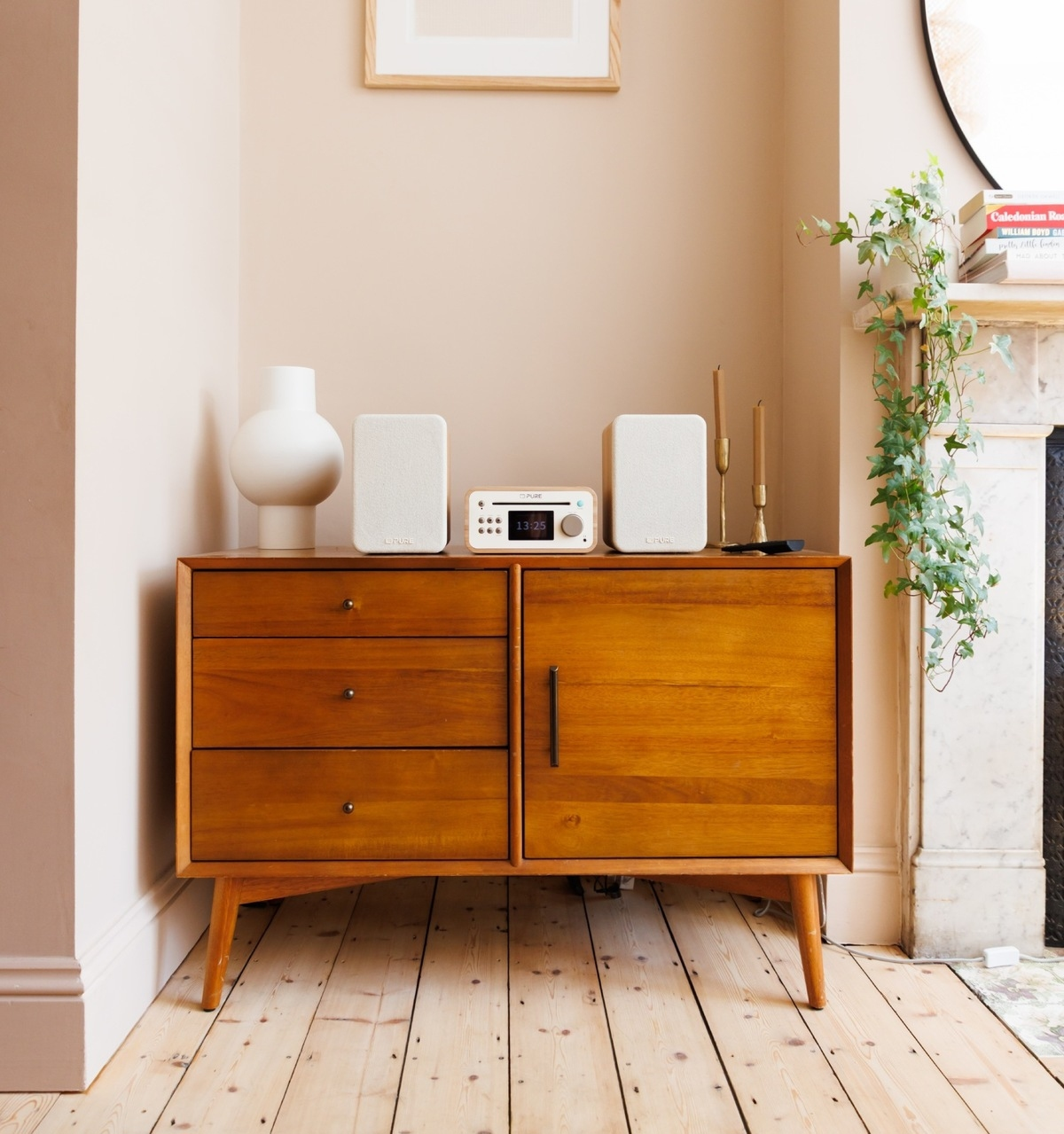 Una cassettiera in legno sostiene un vaso bianco, due altoparlanti bianchi e una radio. Due candele sono vicine.