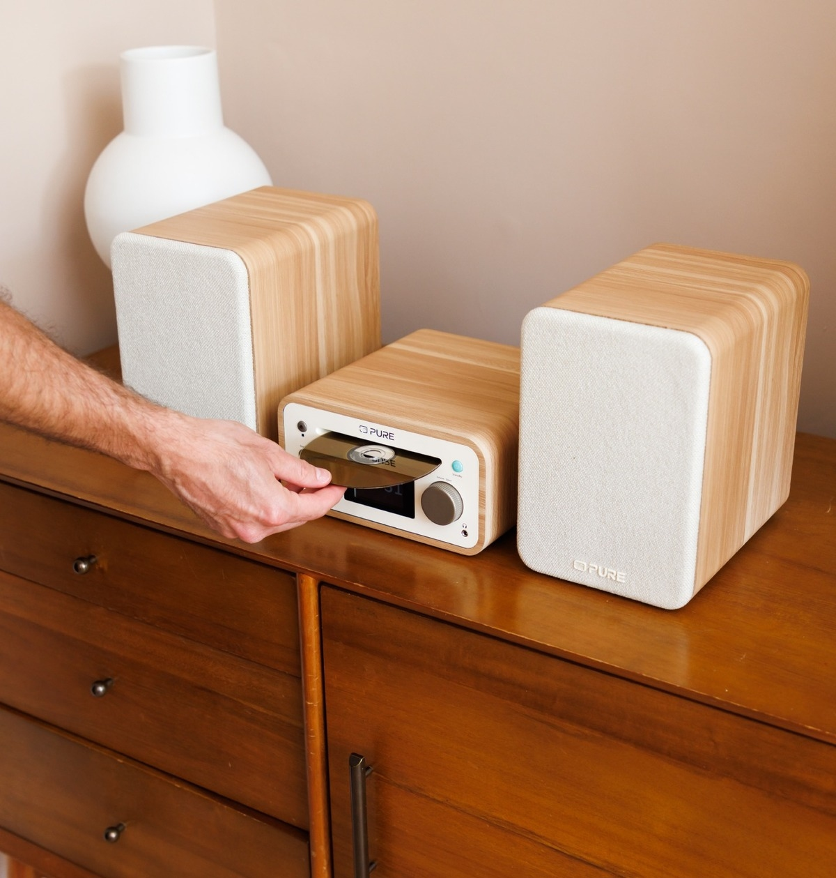 Una mano inserisce un CD in un sistema stereo in legno con altoparlanti bianchi.