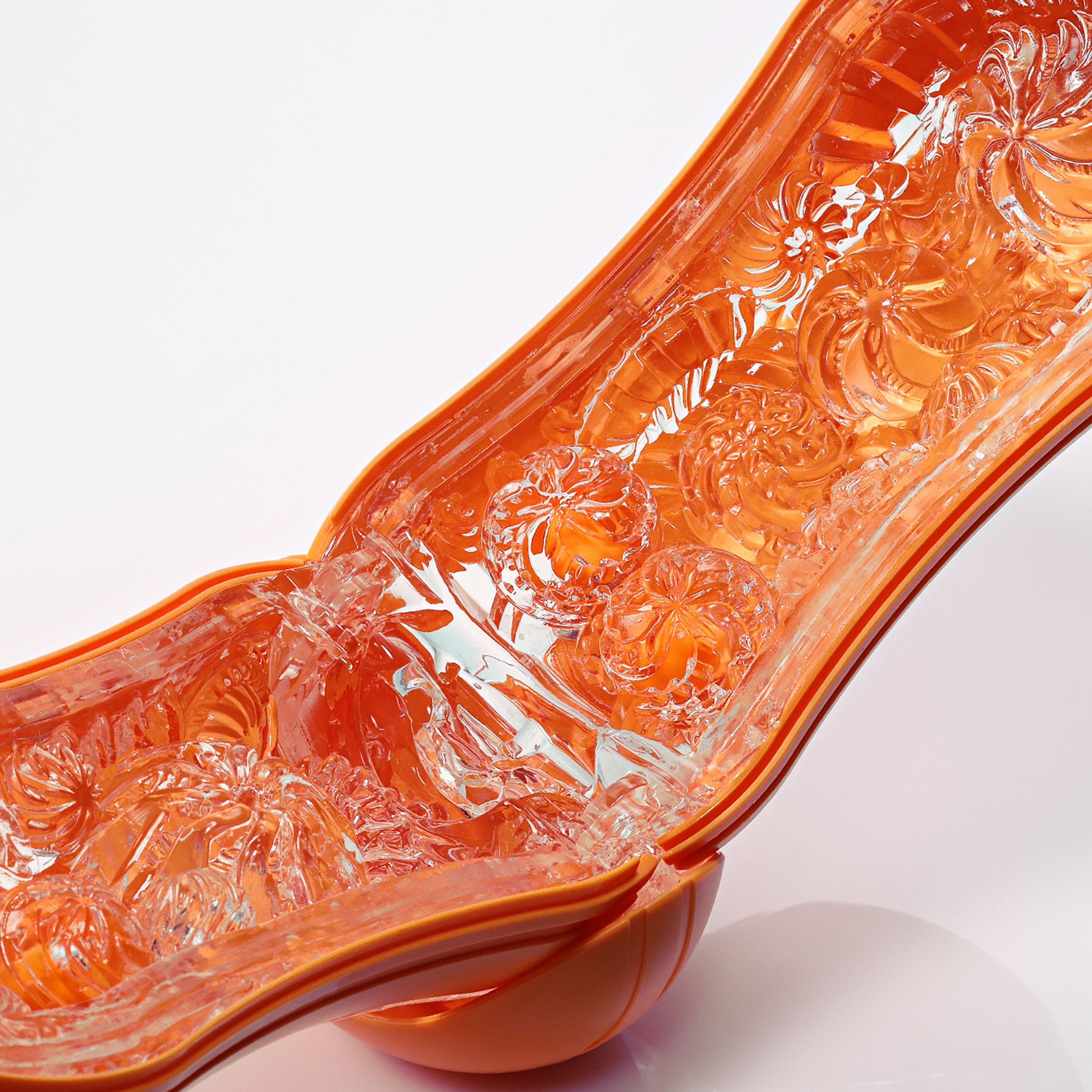 Objeto naranja con patrón floral e insertos transparentes.