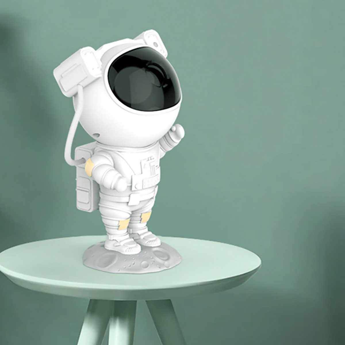 Une figurine d'astronaute blanche se tient sur un socle lunaire gris sur une table vert menthe.