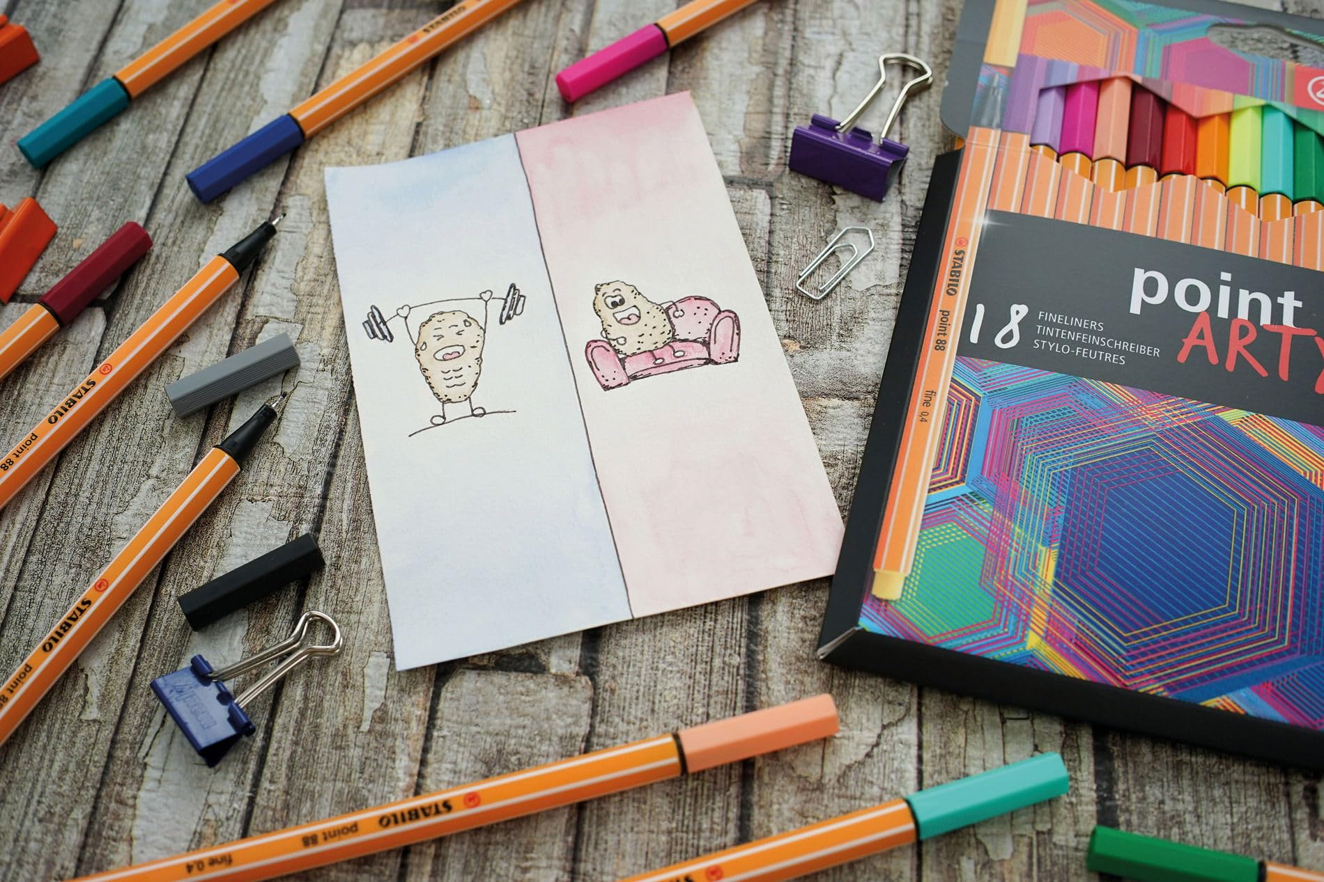 Una vista dall'alto di materiale artistico tra cui penne, una scatola di fineliner e un disegno.