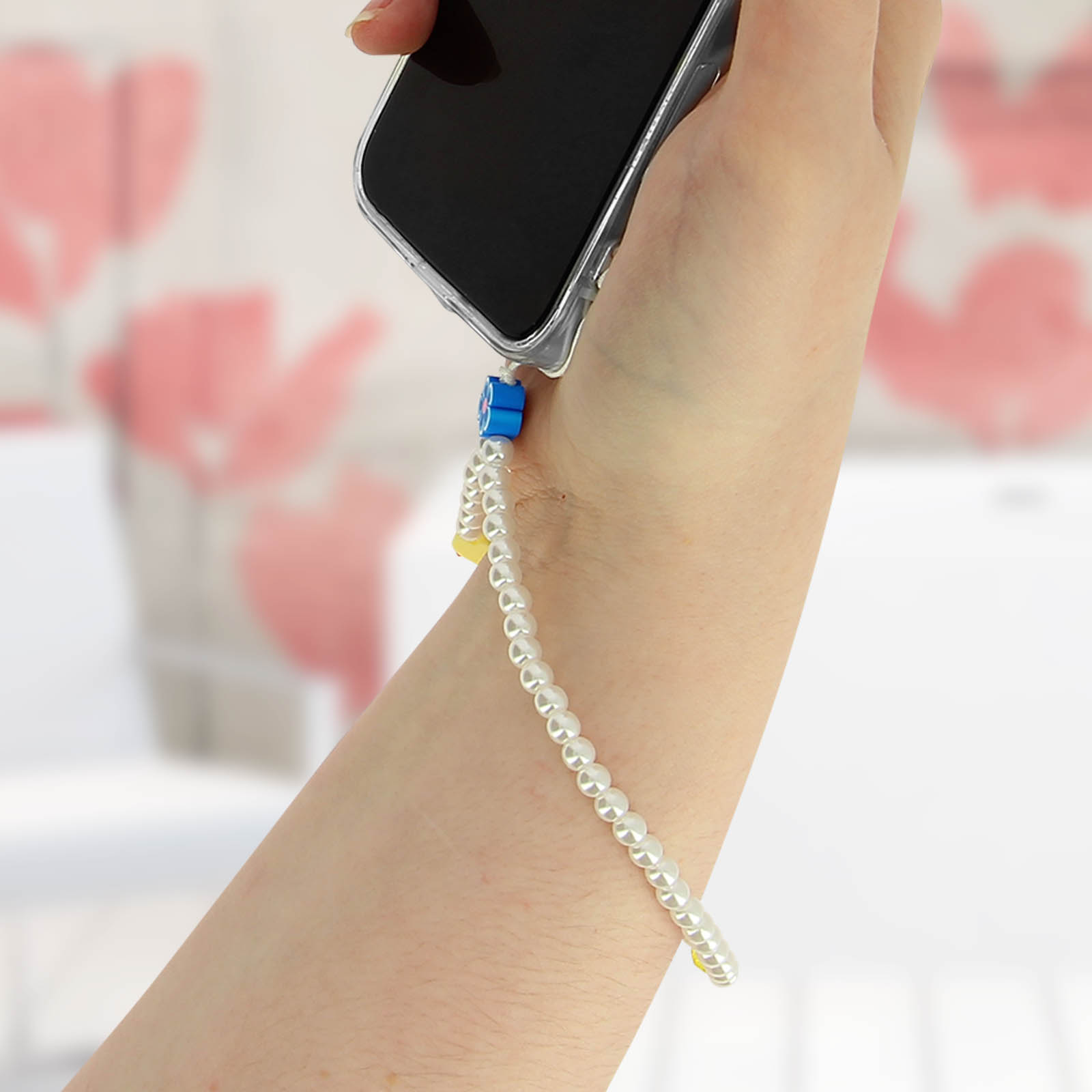 Una mano tiene uno smartphone con un cinturino da polso di perle.