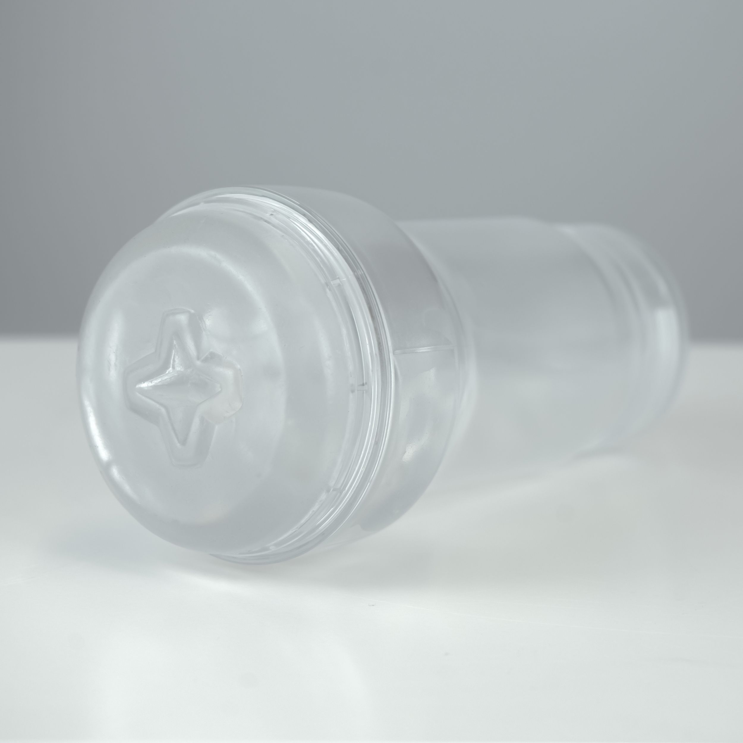 Un recipiente transparente con base en relieve en forma de estrella yace sobre una superficie blanca.