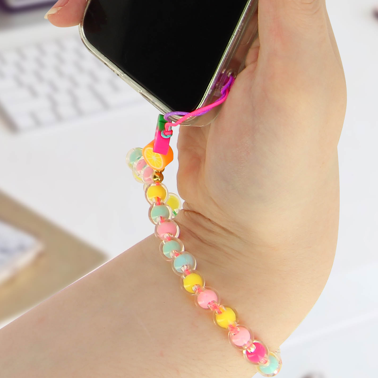 Una mano tiene una custodia trasparente per telefono con un braccialetto di ciondoli colorati e ciondoli di frutta.