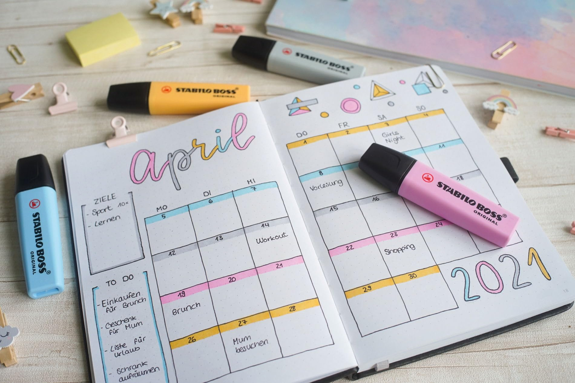 Un taccuino aperto con un calendario di aprile 2021, penne e graffette.