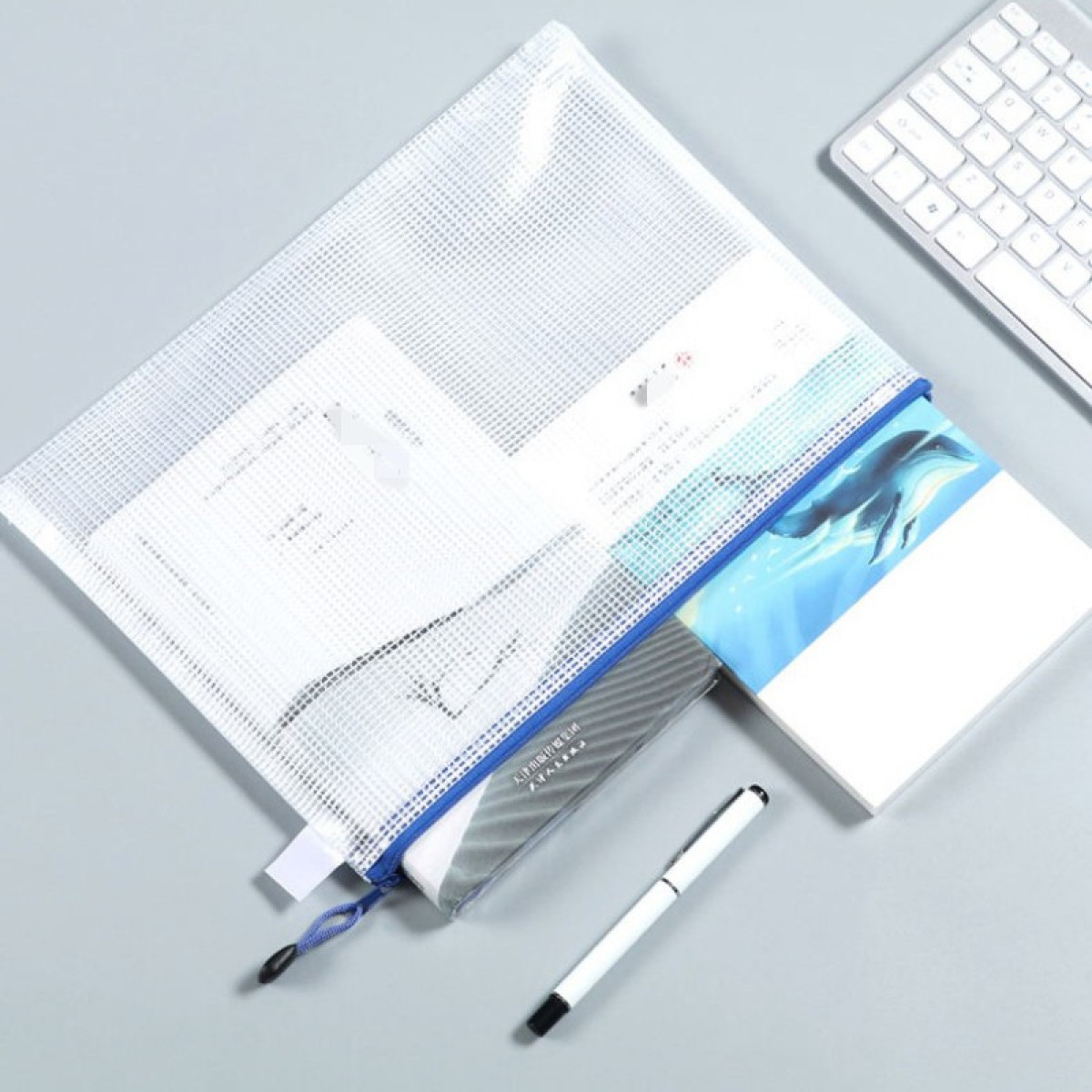 Biała torba na dokumenty z siateczki z papierami, notatnikiem z delfinami, długopisem i klawiaturą.