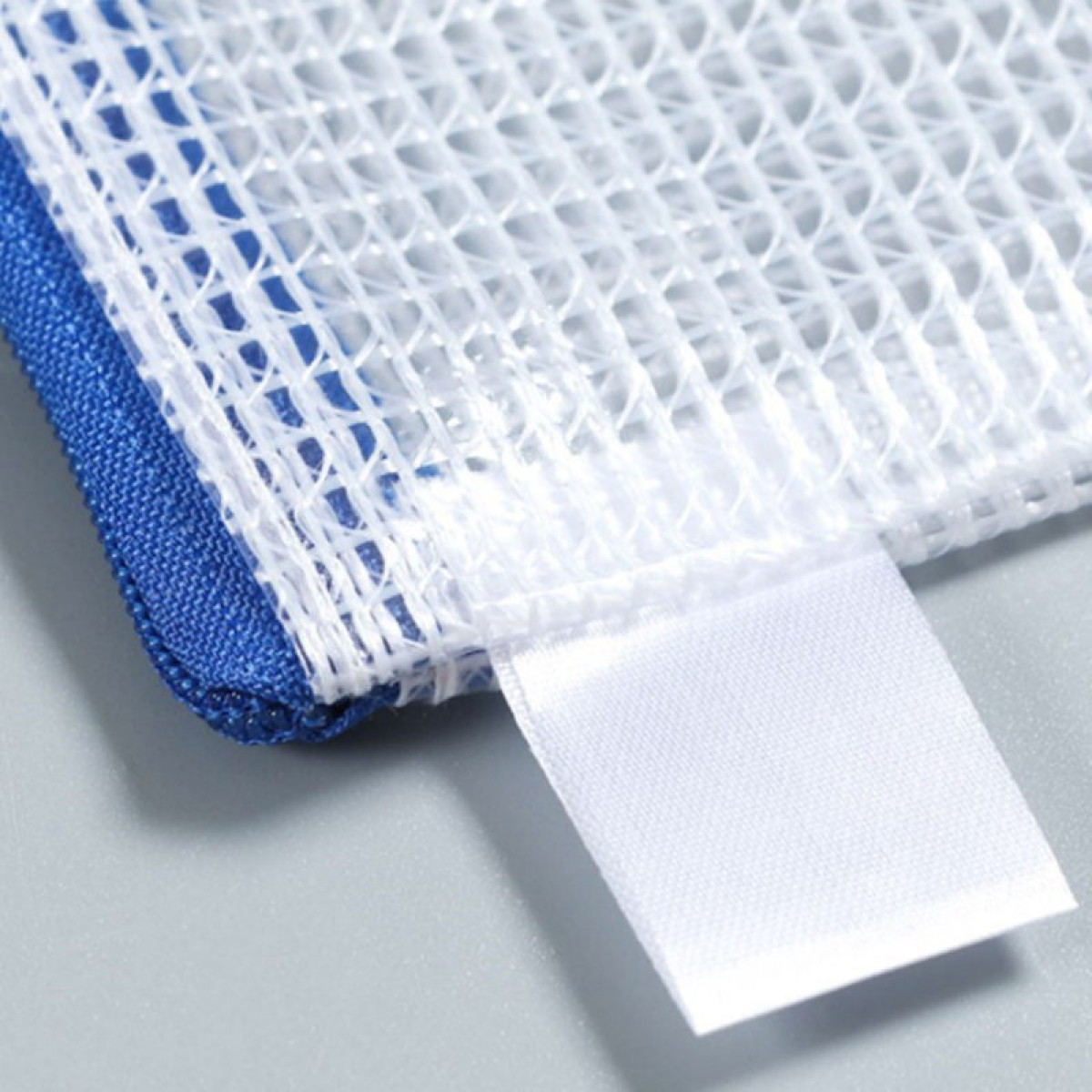 Zbliżenie białej siatkowej torby na pranie z niebieskim obszyciem i pustą białą metką.