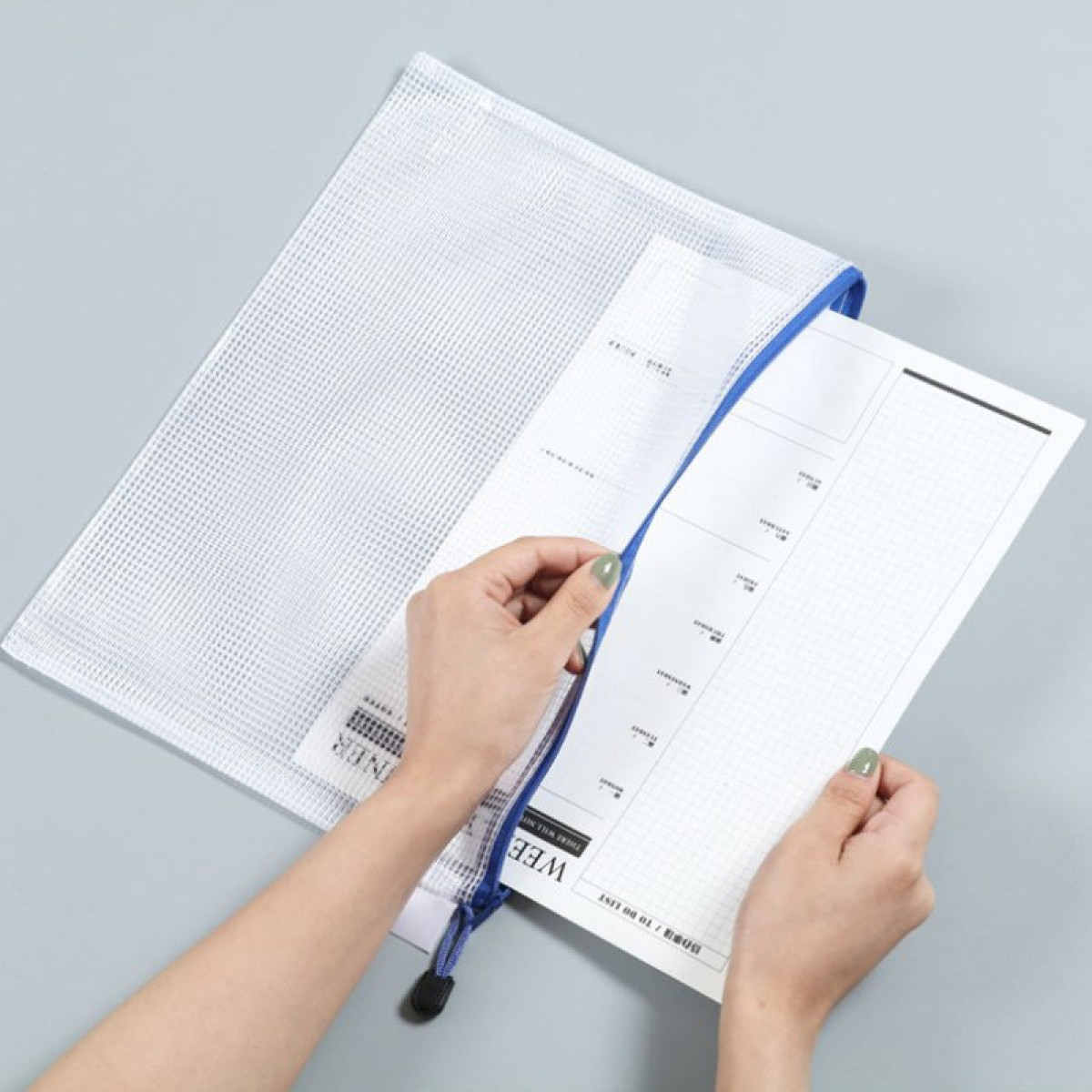 Dłonie wkładają papier do białej, siatkowej saszetki na zamek z niebieskim wykończeniem.