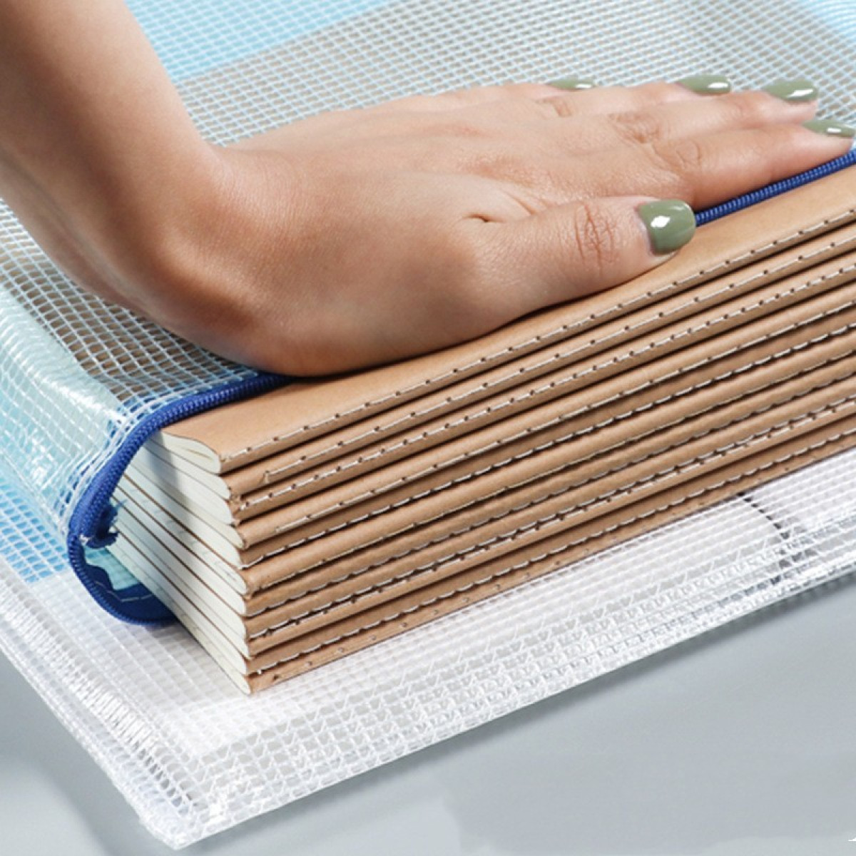 Dłoń spoczywa na stosie notatników w przezroczystej torbie.