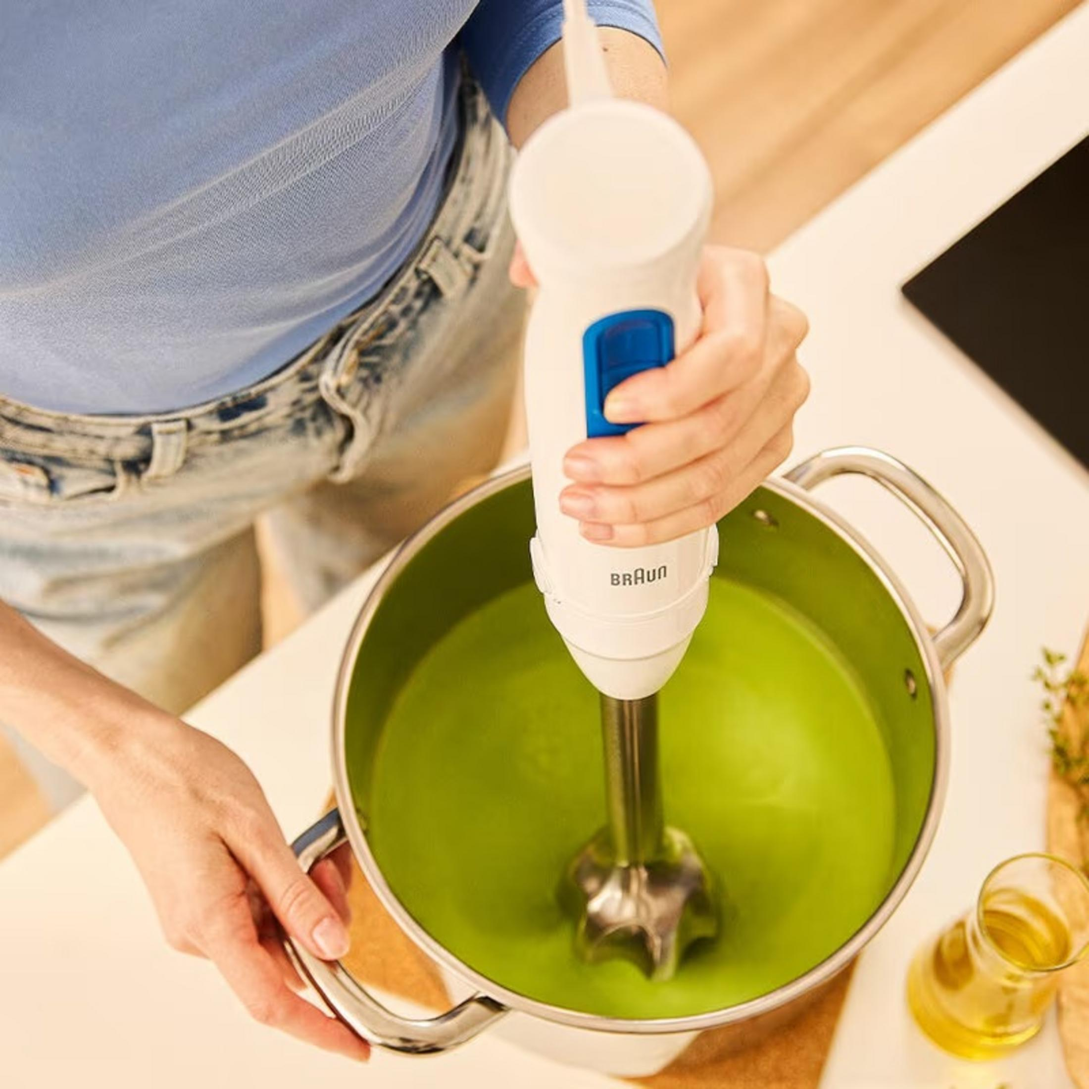Una persona frulla zuppa verde in una pentola con un frullatore a immersione Braun bianco.