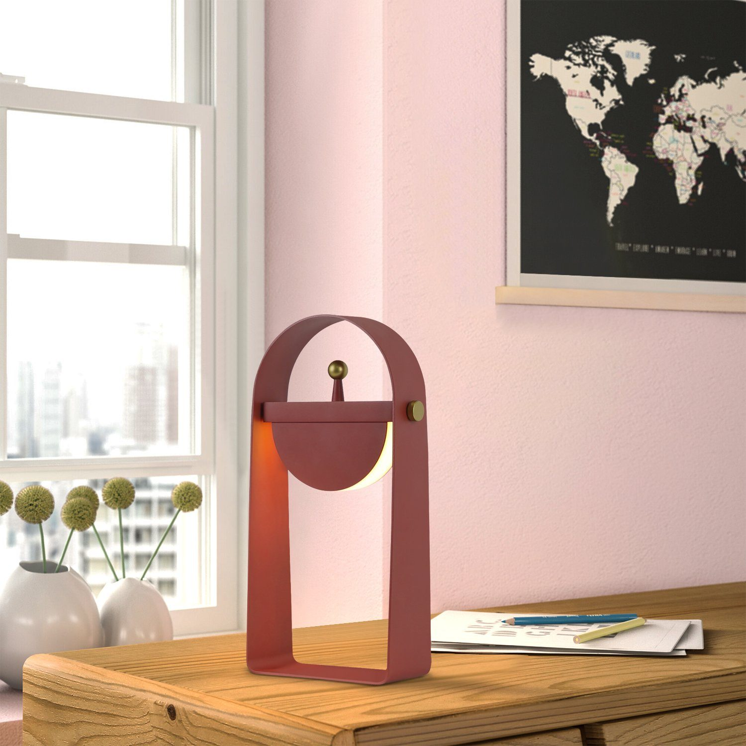 Una lampada rossa su una scrivania di legno vicino a una finestra con vista sulla città.