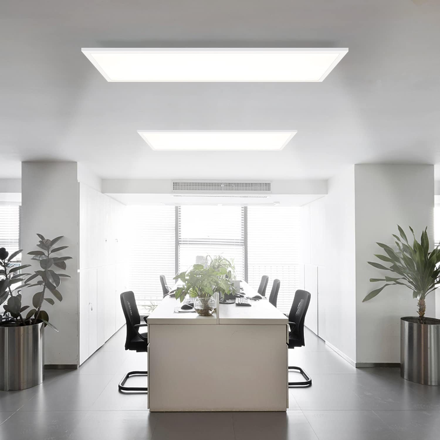 Ufficio moderno con scrivanie bianche, sedie, piante e grandi luci a soffitto.