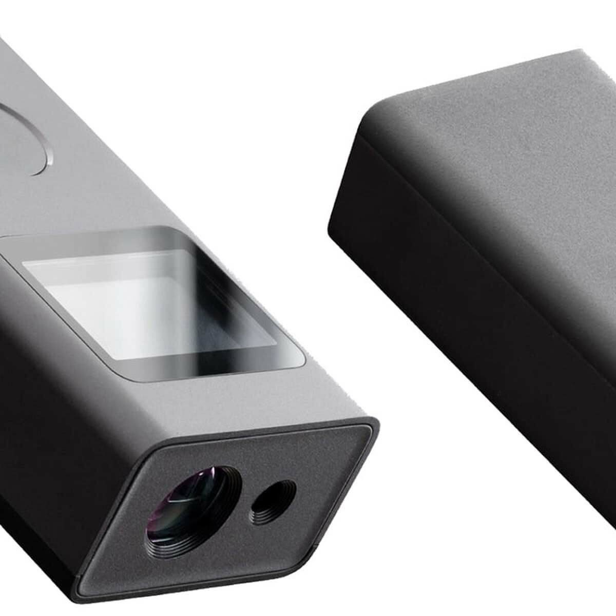 Primo piano di un dispositivo digitale grigio con schermo e lente, accanto a un oggetto rettangolare nero.