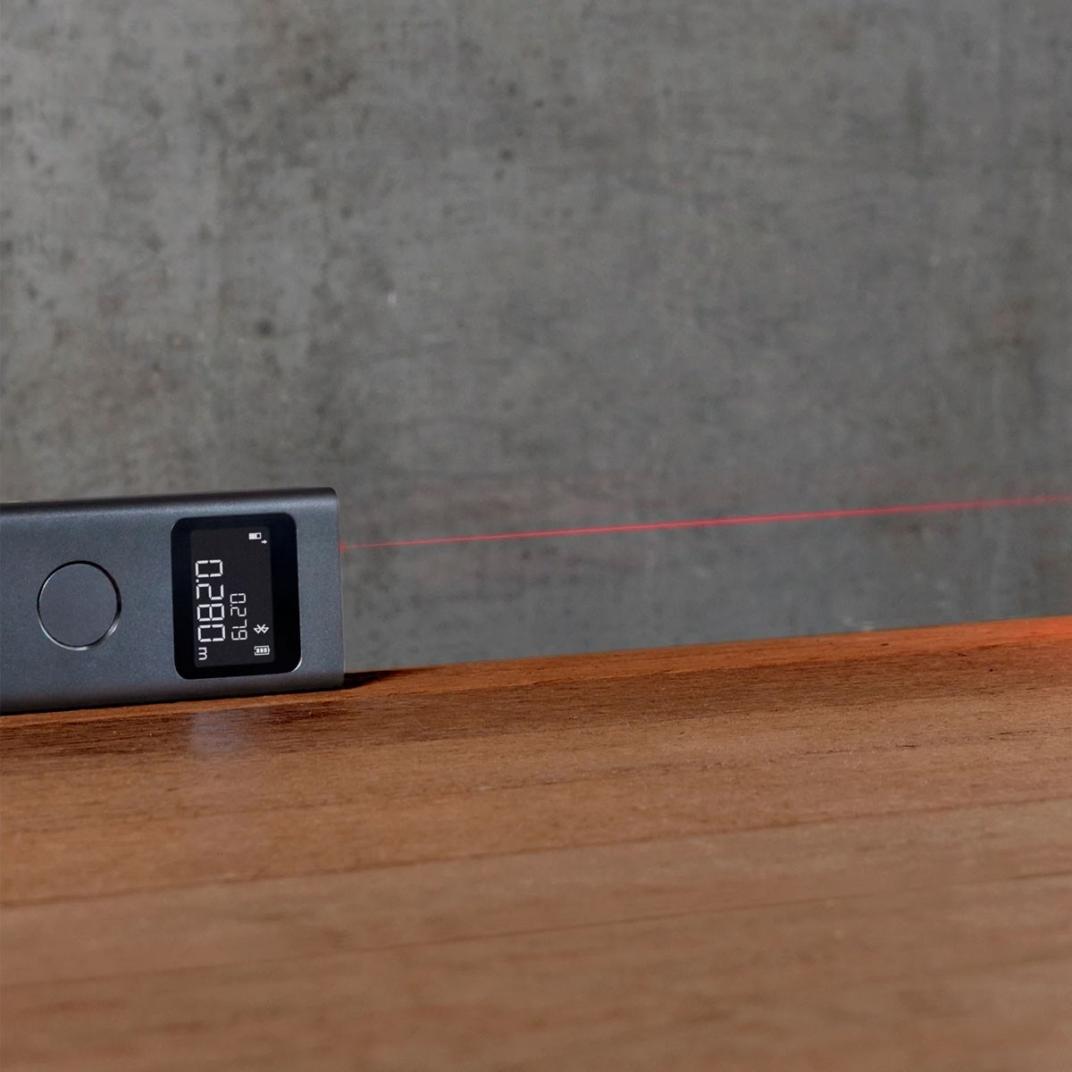 Un dispositivo di misurazione laser grigio scuro su una superficie di legno emette una sottile linea laser rossa.