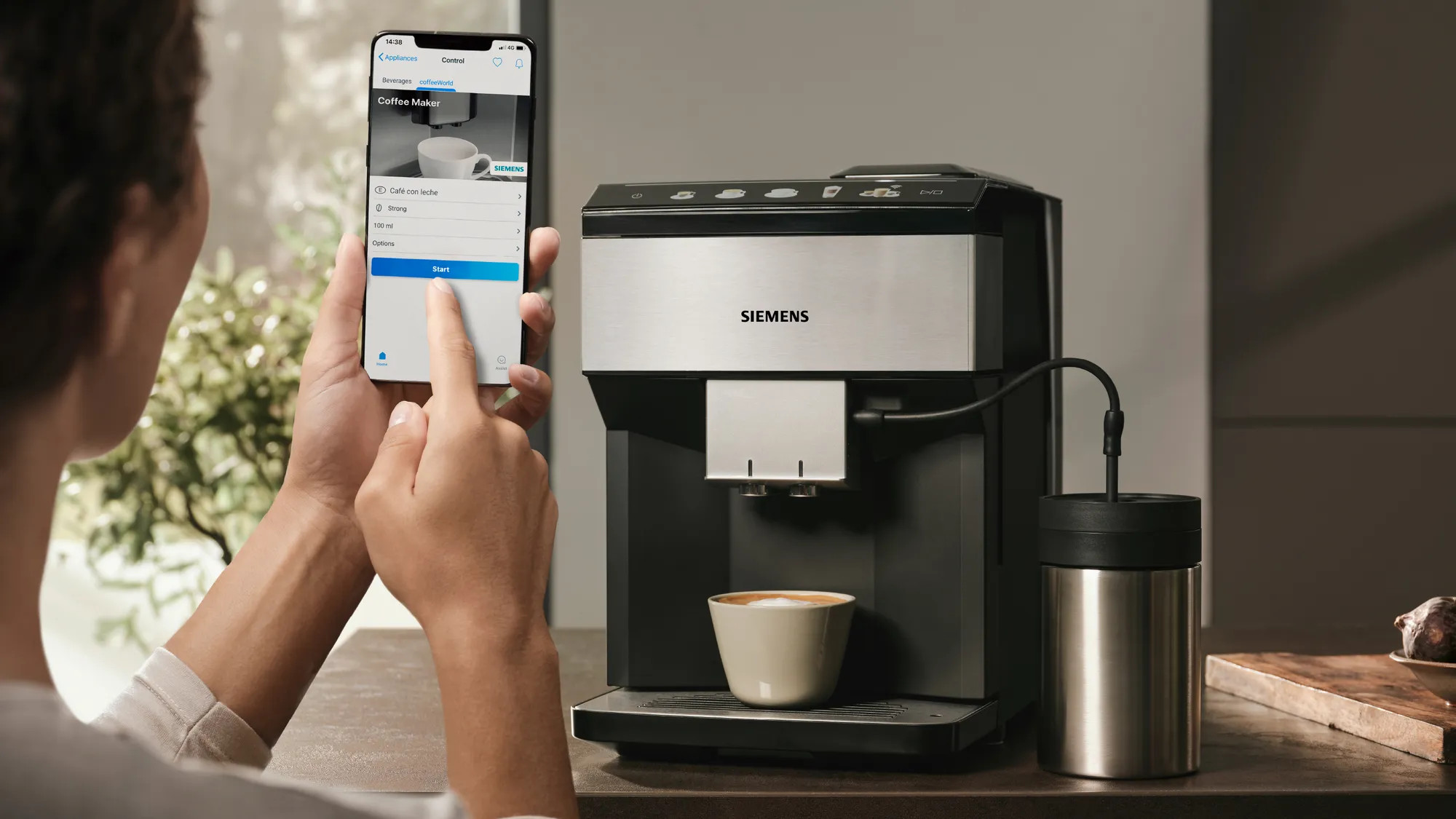Una persona controlla una macchina da caffè tramite smartphone con un'app Siemens.