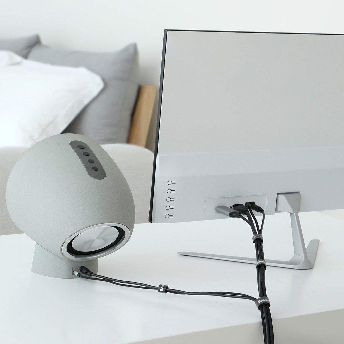 Un altoparlante grigio a sinistra di un monitor. Cavi li collegano. Letto sullo sfondo.